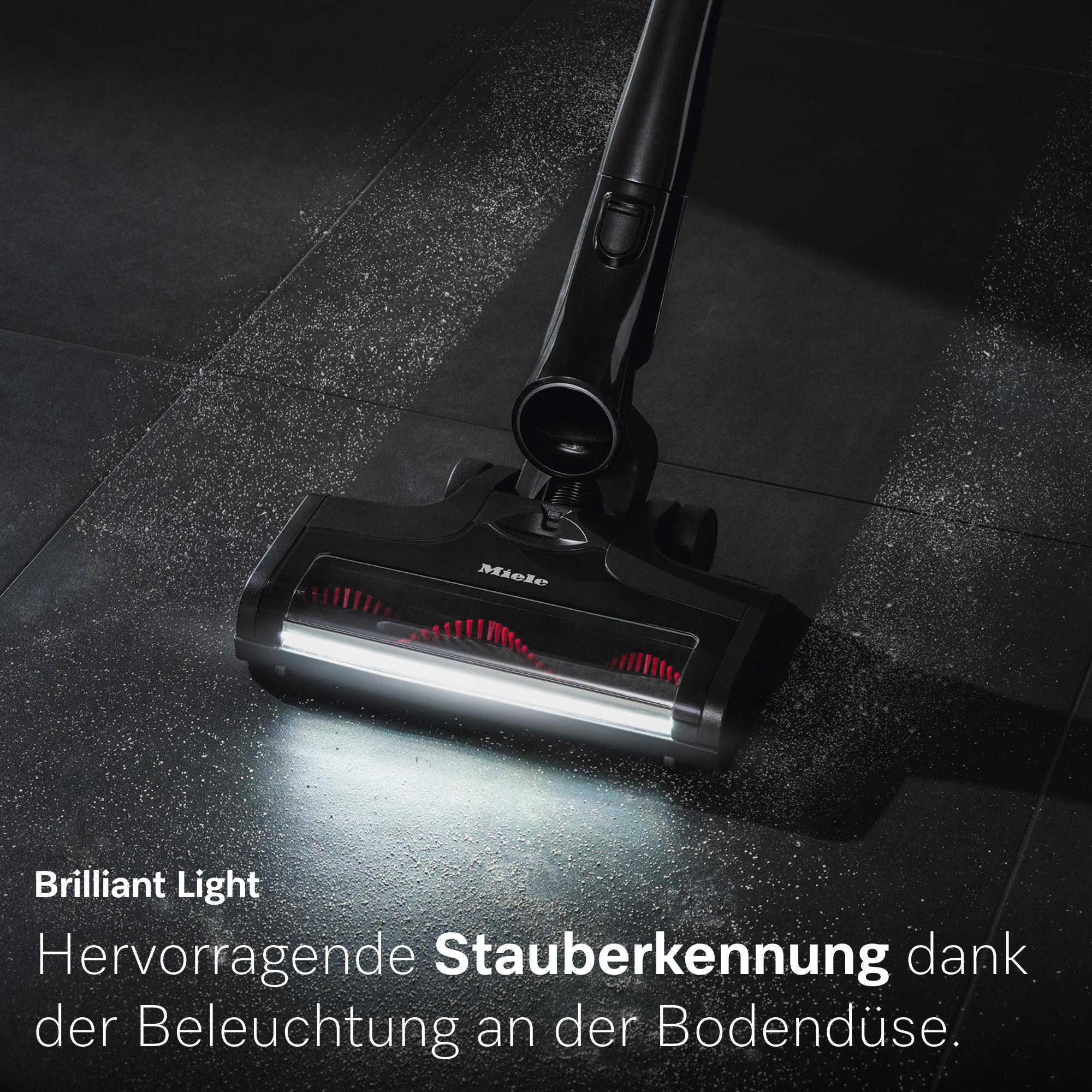 Schwarzer Staubsauger mit heller Bodendüse reinigt schmutzige dunkle Fliesen.