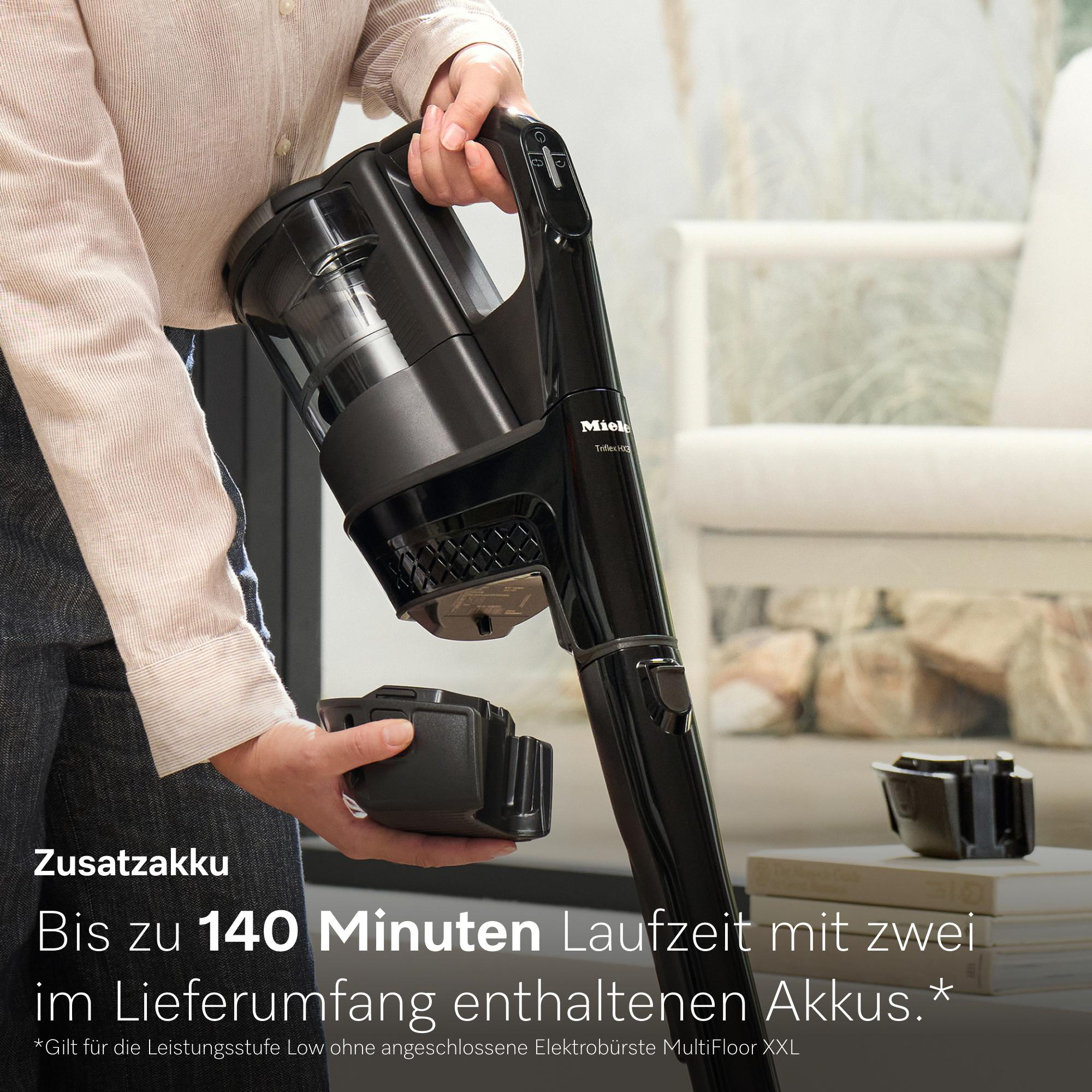 Eine Person hält einen schwarzen Akku für einen Staubsauger. Im Hintergrund ist ein Sofa.