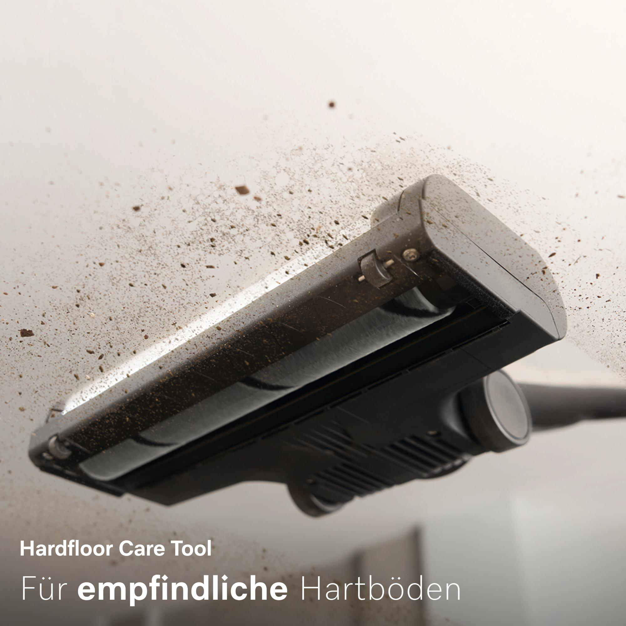Dreck wirbelt auf, während ein schwarzer Hartbodenreiniger auf einem hellen Boden arbeitet.