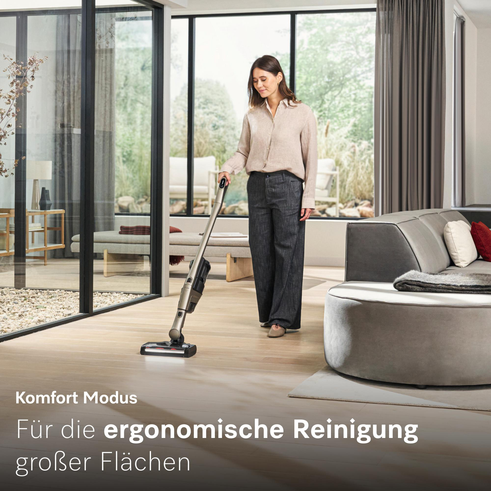 Frau saugt mit einem Akku-Staubsauger auf hellem Holzboden in einem modernen Wohnzimmer.