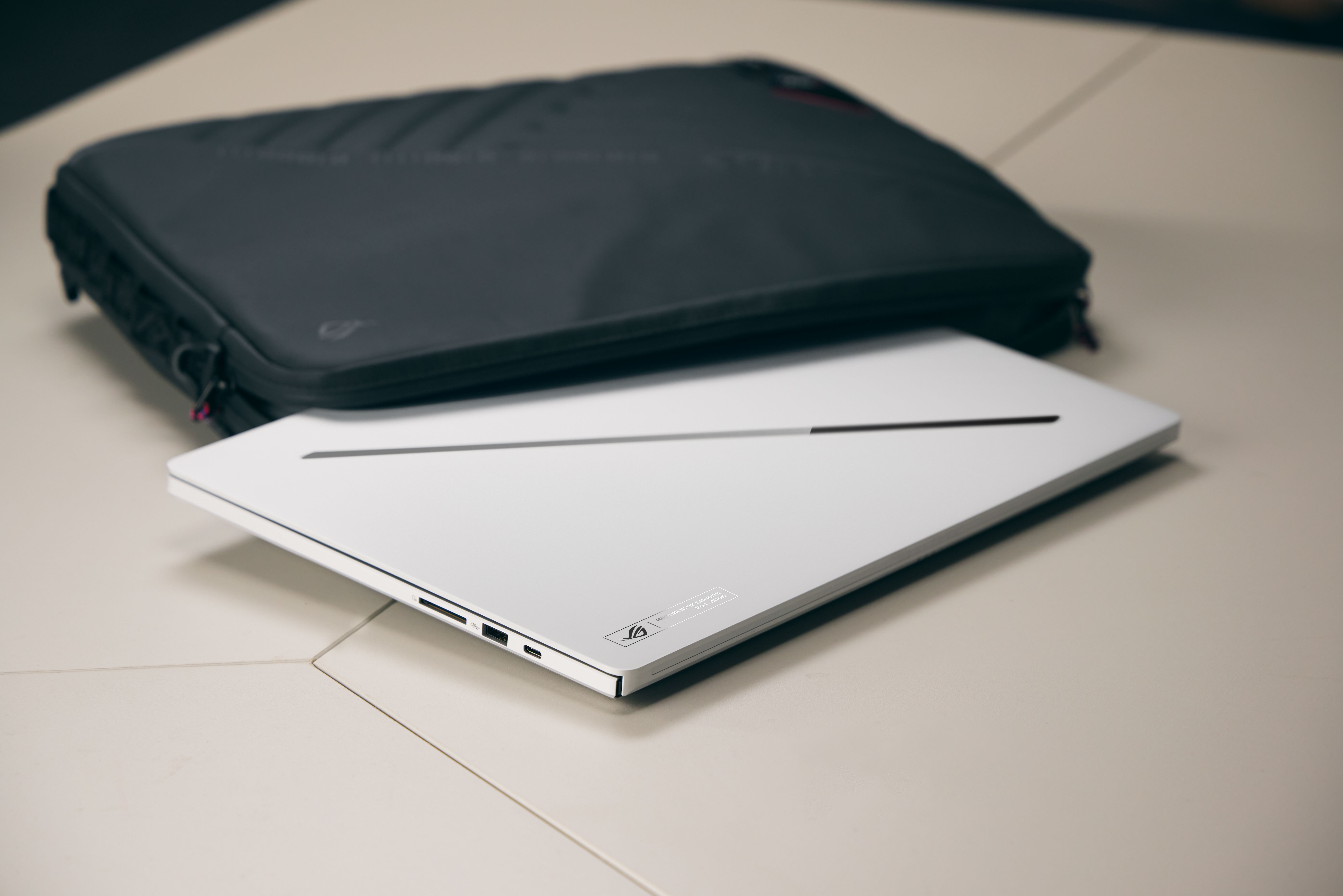 Ein weißer Laptop liegt unter einer schwarzen Laptoptasche auf einem Tisch.