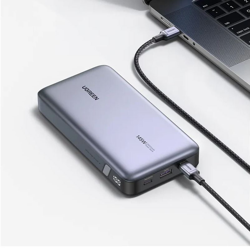 Grauer UGREEN Powerbank mit 145W lädt Laptop über USB-C Kabel. Anzeige zeigt 100%.