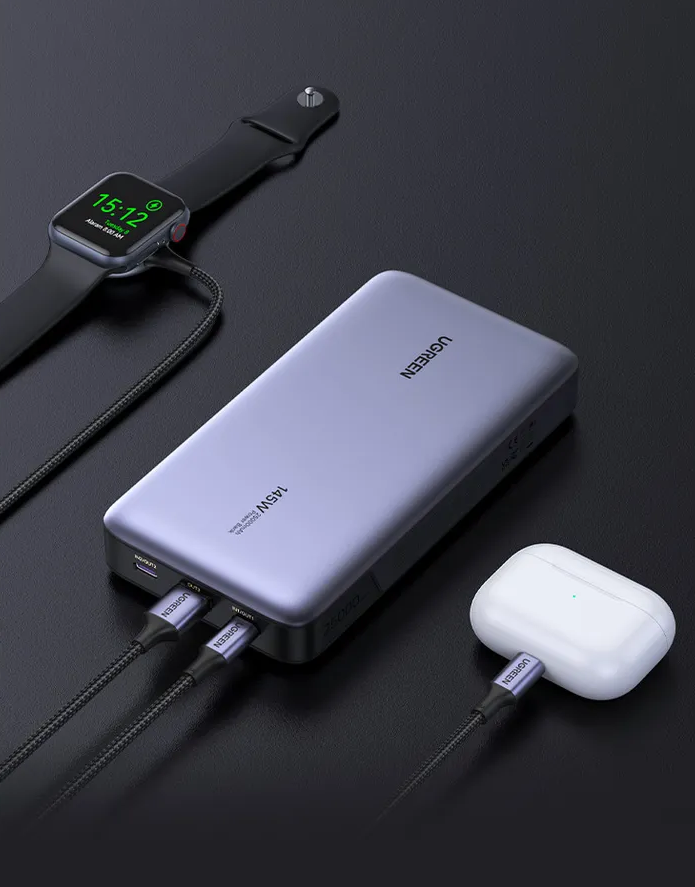 Eine silberne Powerbank lädt eine Apple Watch und weiße Ohrhörer. Kabel verbinden sie.