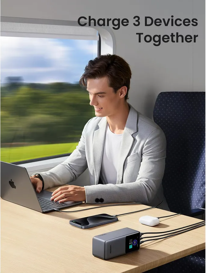 Uomo carica laptop, telefono e auricolari su un treno con power bank.