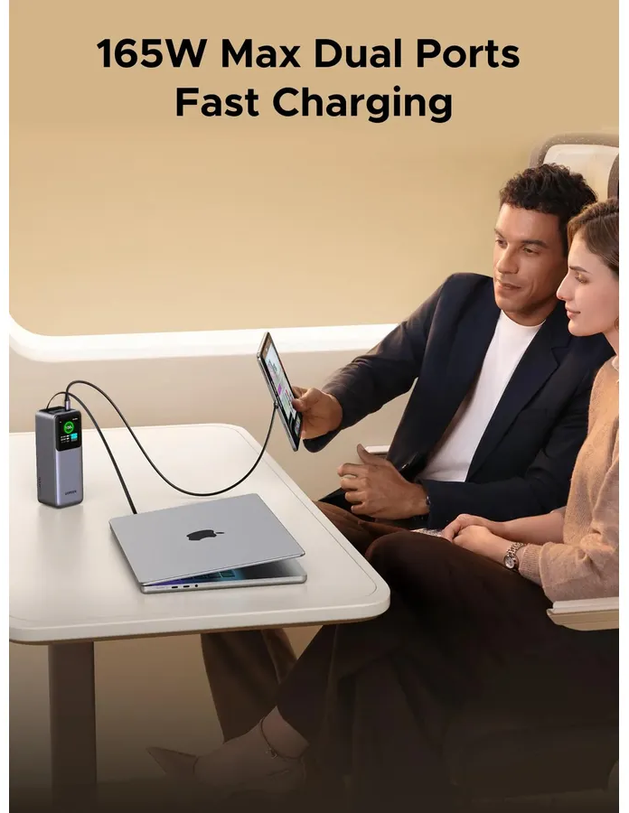 Ein graues Ladegerät versorgt einen Laptop und ein Tablet auf einem Tisch. Zwei Personen sitzen.