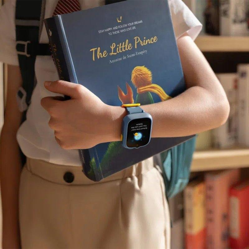 Una persona sostiene el libro "El Principito" con un smartwatch azul con cara de caricatura en la pantalla.