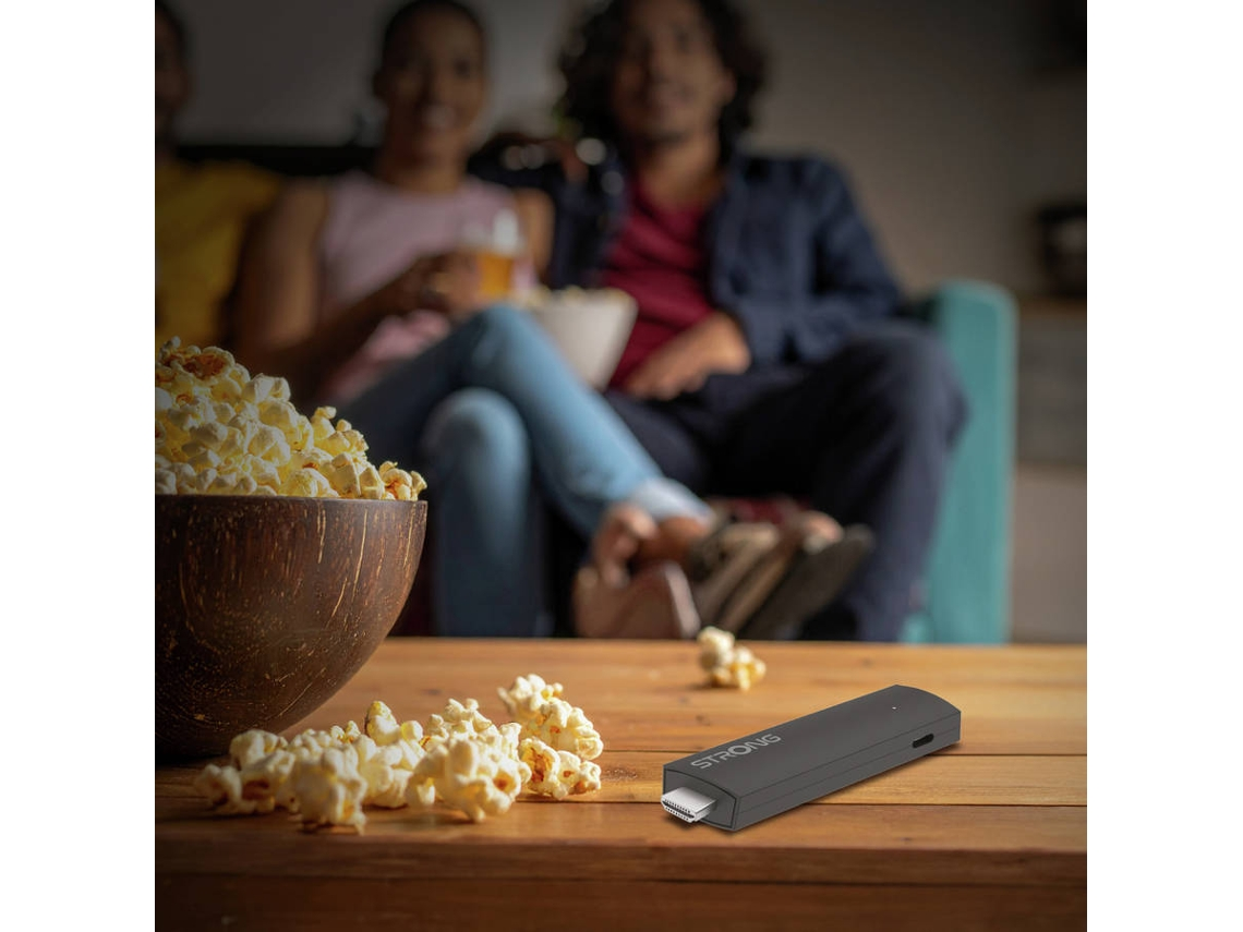 Un stick de streaming negro descansa en una mesa de madera junto a un bol de palomitas.