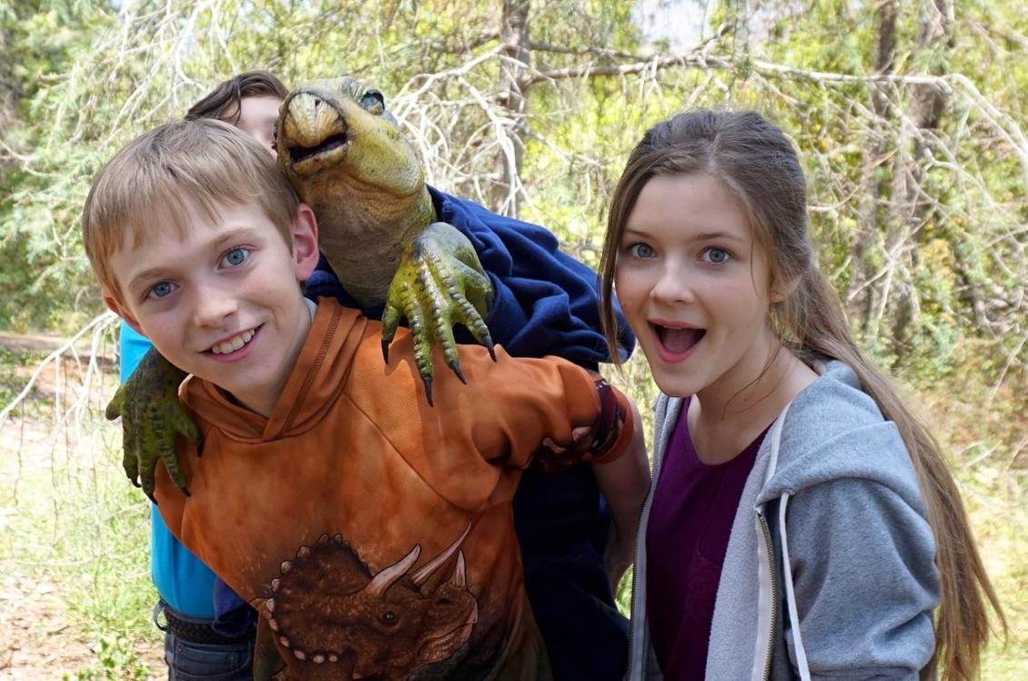 Zwei Kinder und eine Dinosaurierpuppe posieren im Freien.