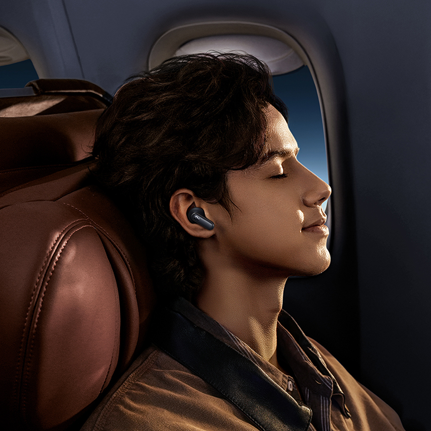 Hombre con audífonos duerme en avión, interior oscuro, atardecer afuera.