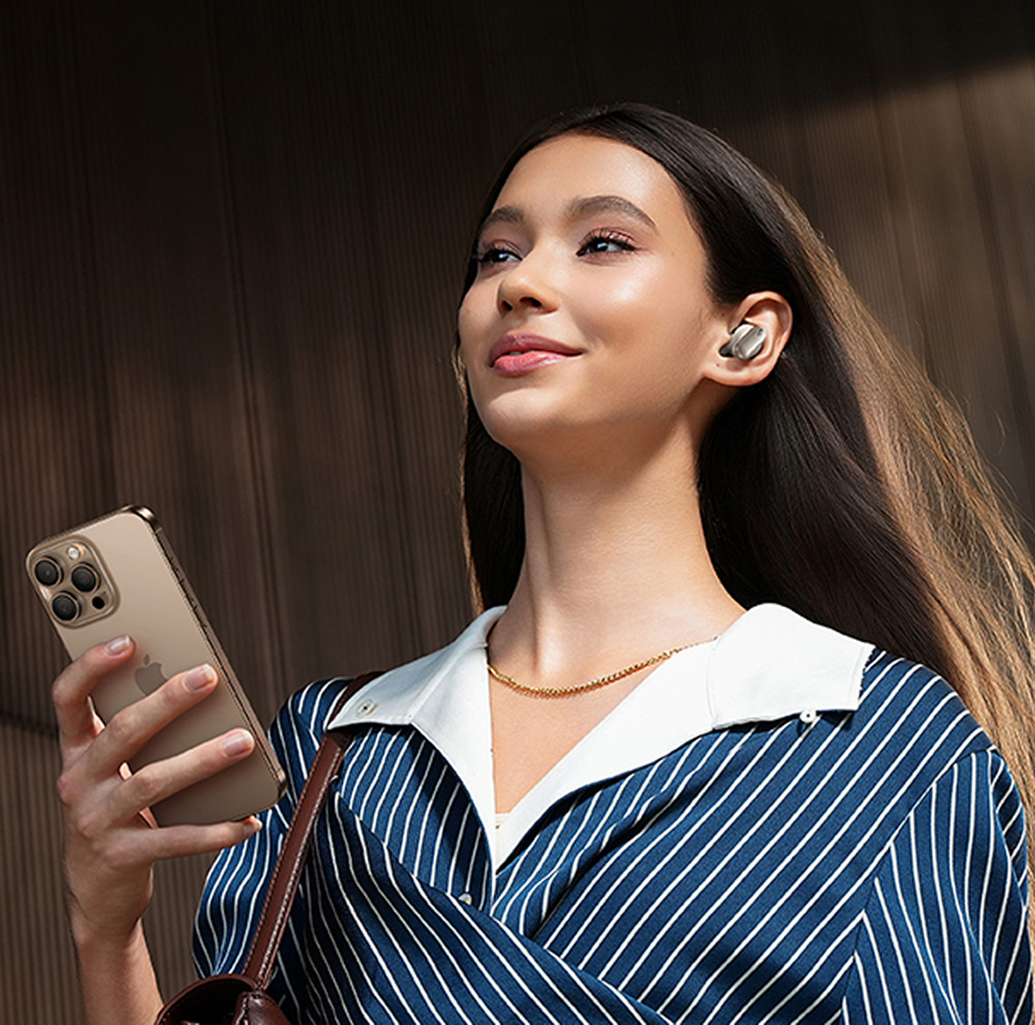 Mujer joven con auriculares y teléfono frente a fondo marrón.