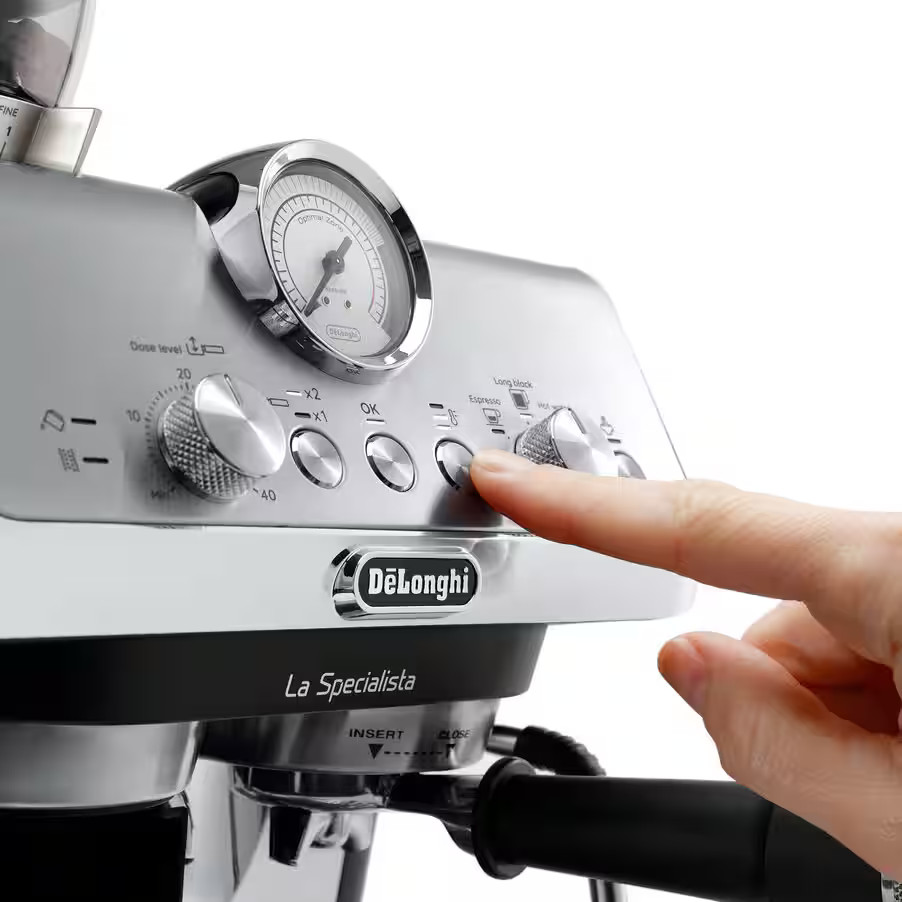 Palec naciska przycisk na srebrnej maszynie do espresso DeLonghi La Specialista z manometrem.
