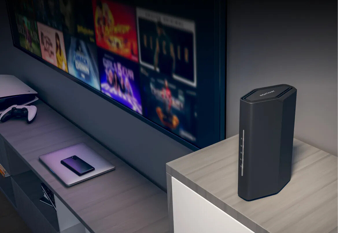 Czarny router stoi na stole przed ekranem telewizora wyświetlającym filmy.
