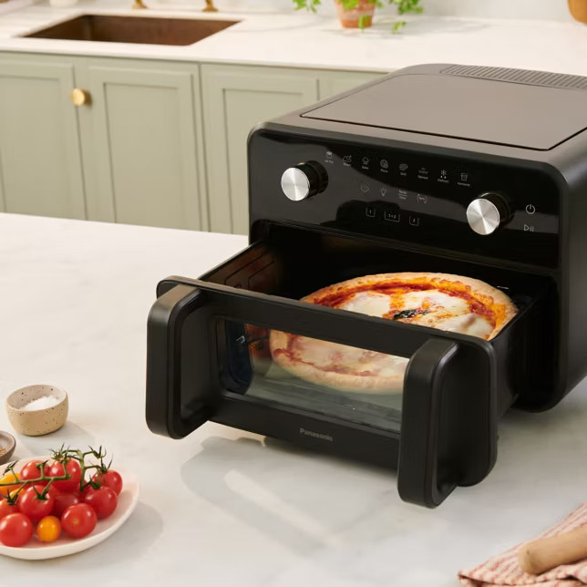 Czarna frytkownica beztłuszczowa z pizzą w środku na blacie kuchennym.