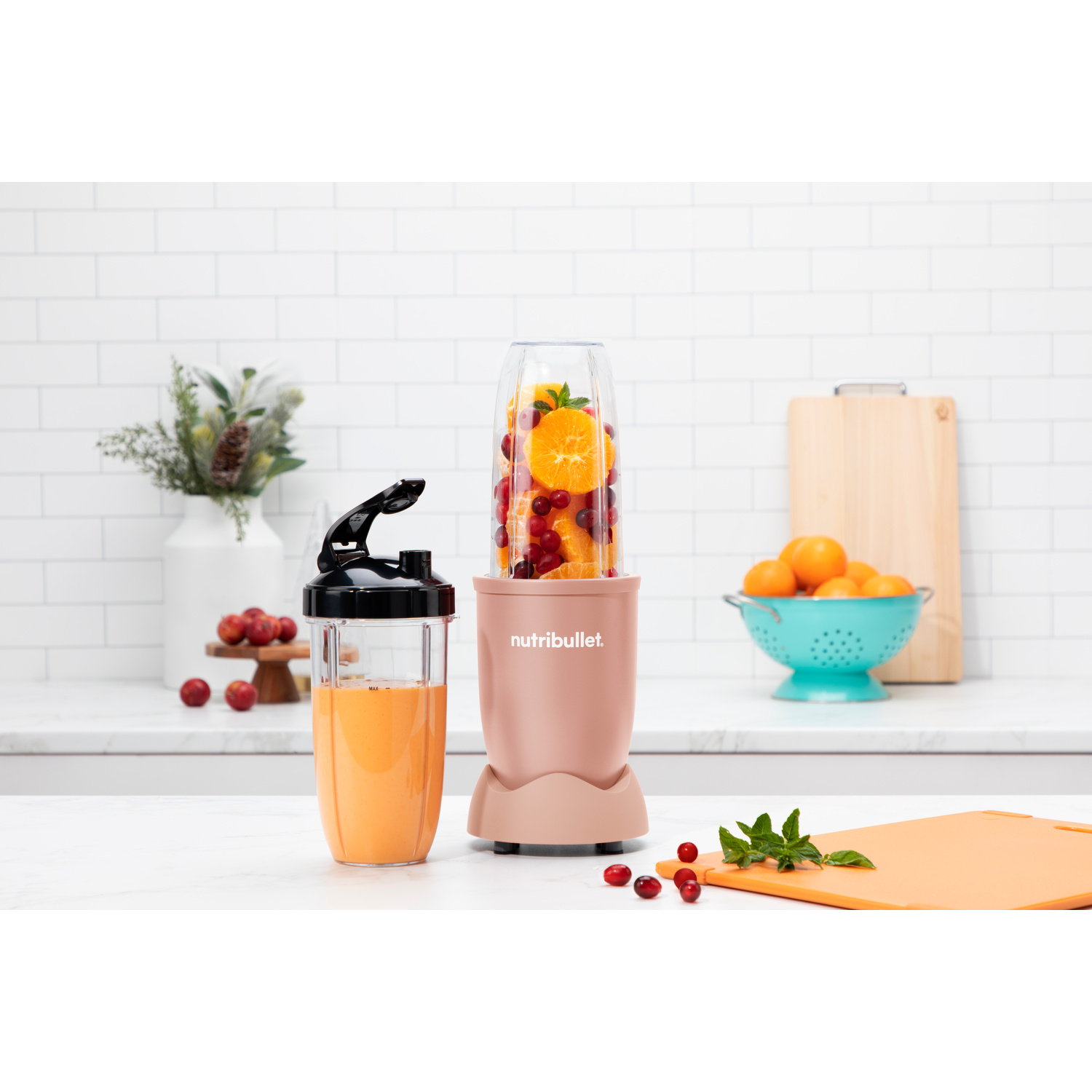 Un frullatore rosa su un piano di lavoro con una tazza di succo e frutta.