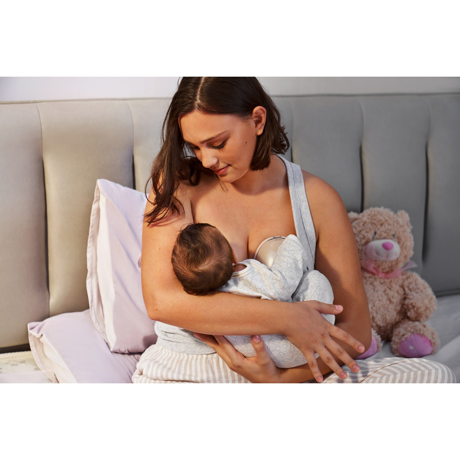 Een vrouw voedt haar baby in bed, een teddybeer zit ernaast.