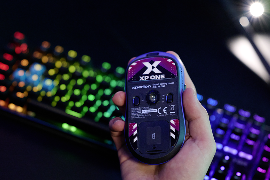 Egy kéz lila gamer egeret tart egy színes billentyűzet előtt.