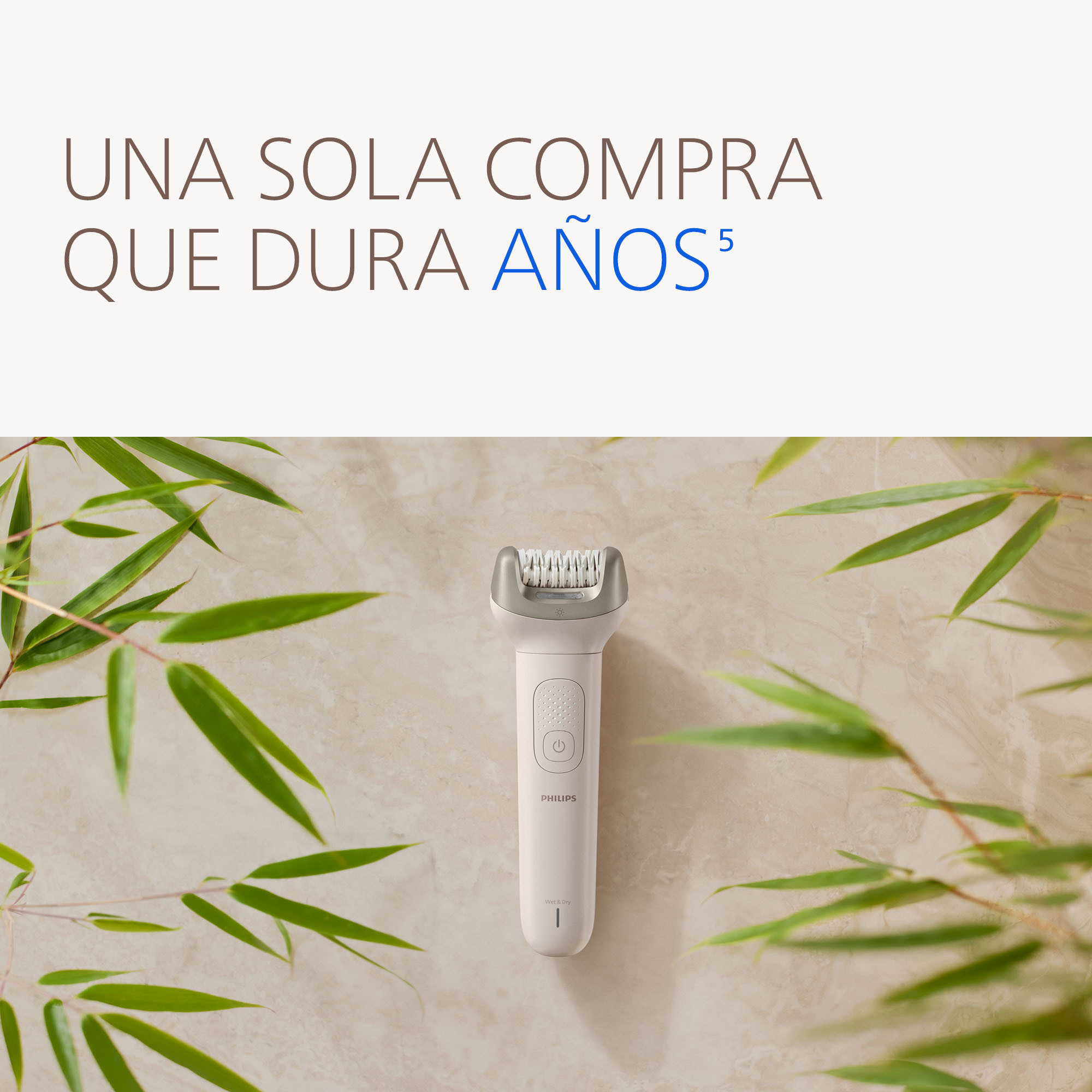 Un depilador Philips blanco con cabezal plateado sobre mármol claro, rodeado de hojas de bambú.