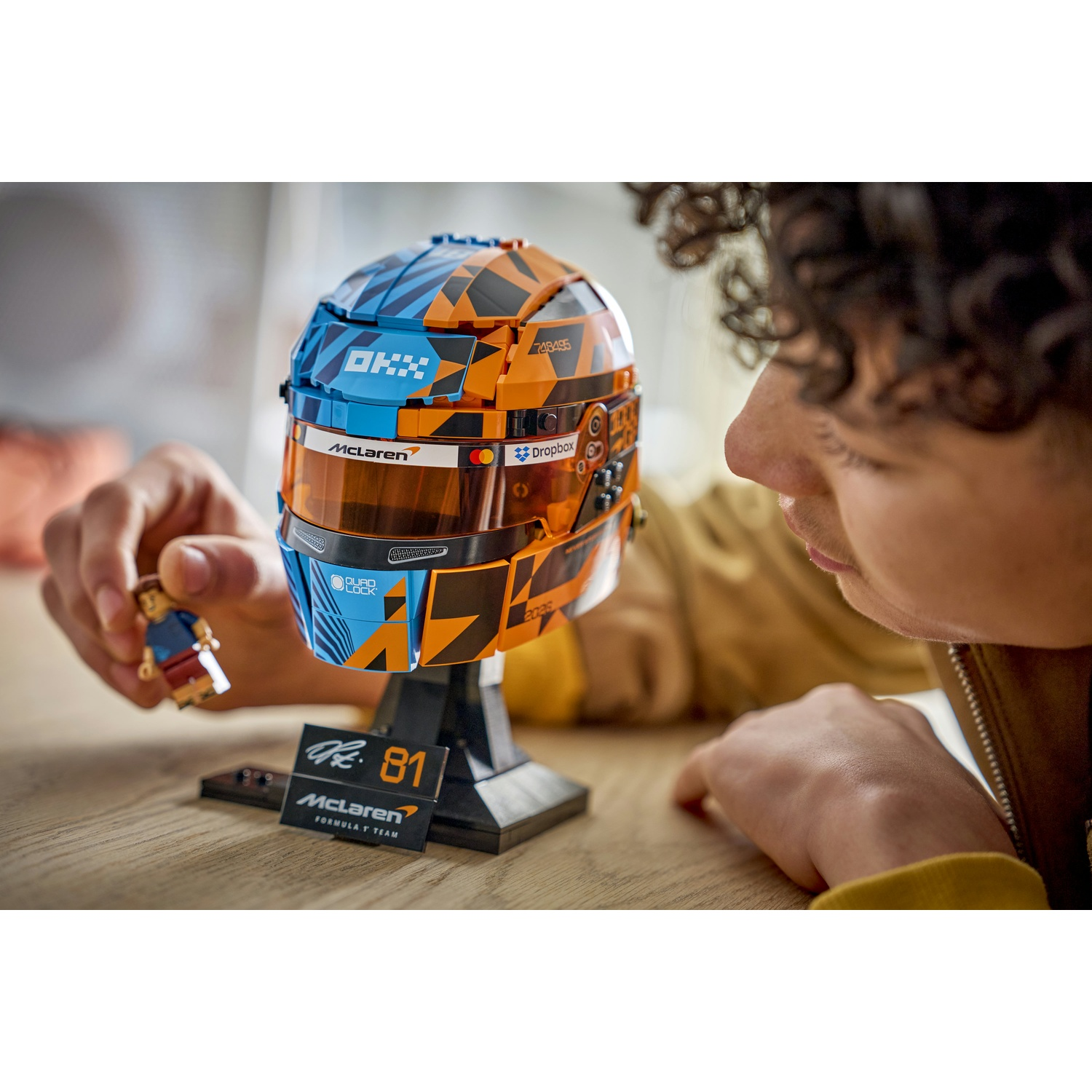 Un ragazzo guarda un casco Lego McLaren arancione e blu. Tiene una piccola figura.