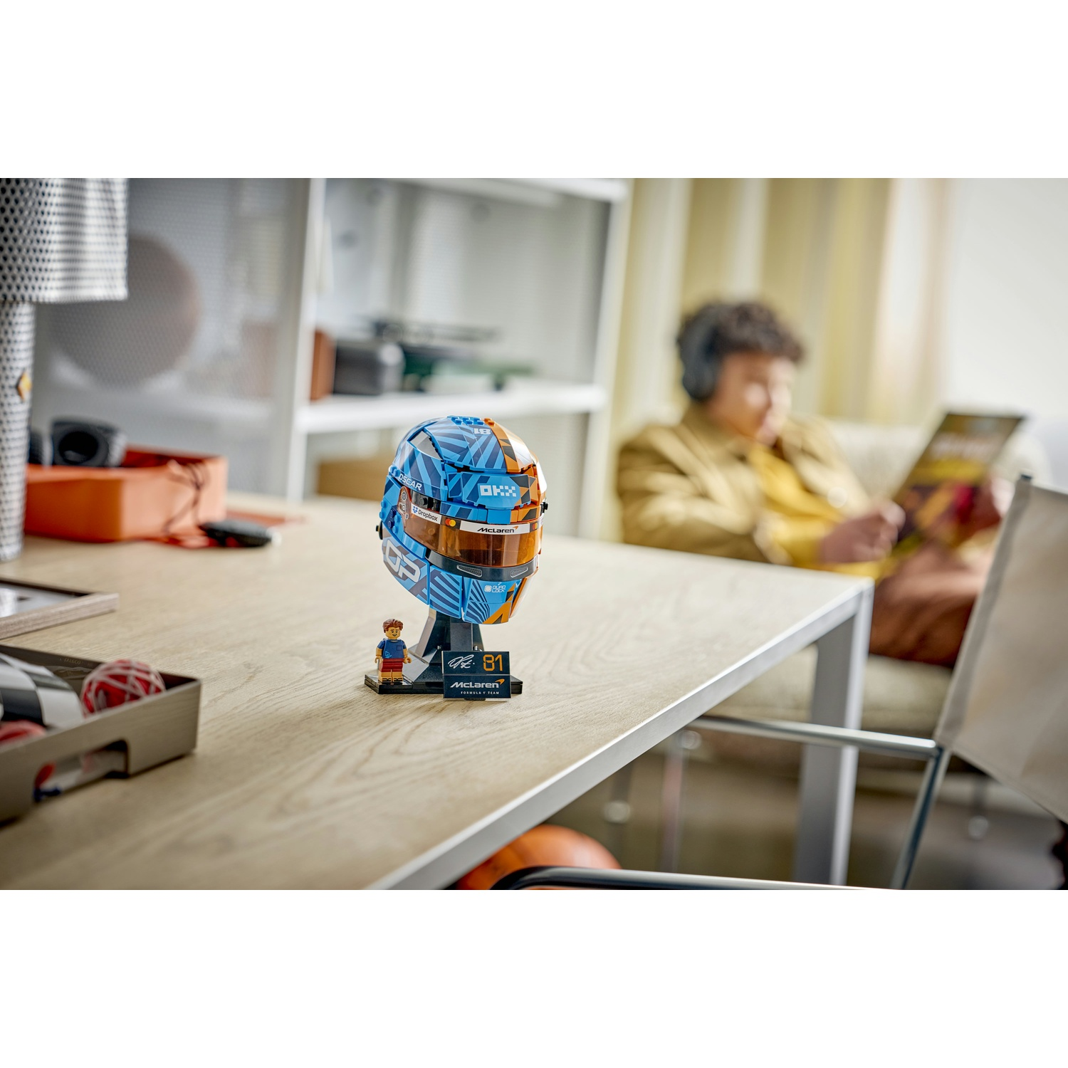 Modello di casco Lego McLaren su un tavolo con una persona che legge sullo sfondo.