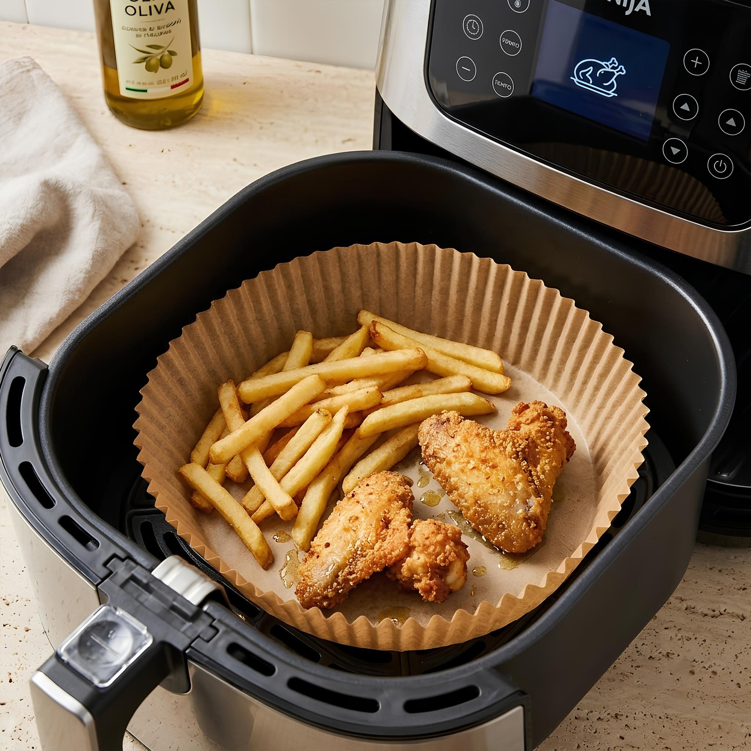 Patatine fritte e alette di pollo in friggitrice ad aria su carta forno, accanto a una bottiglia d'olio.