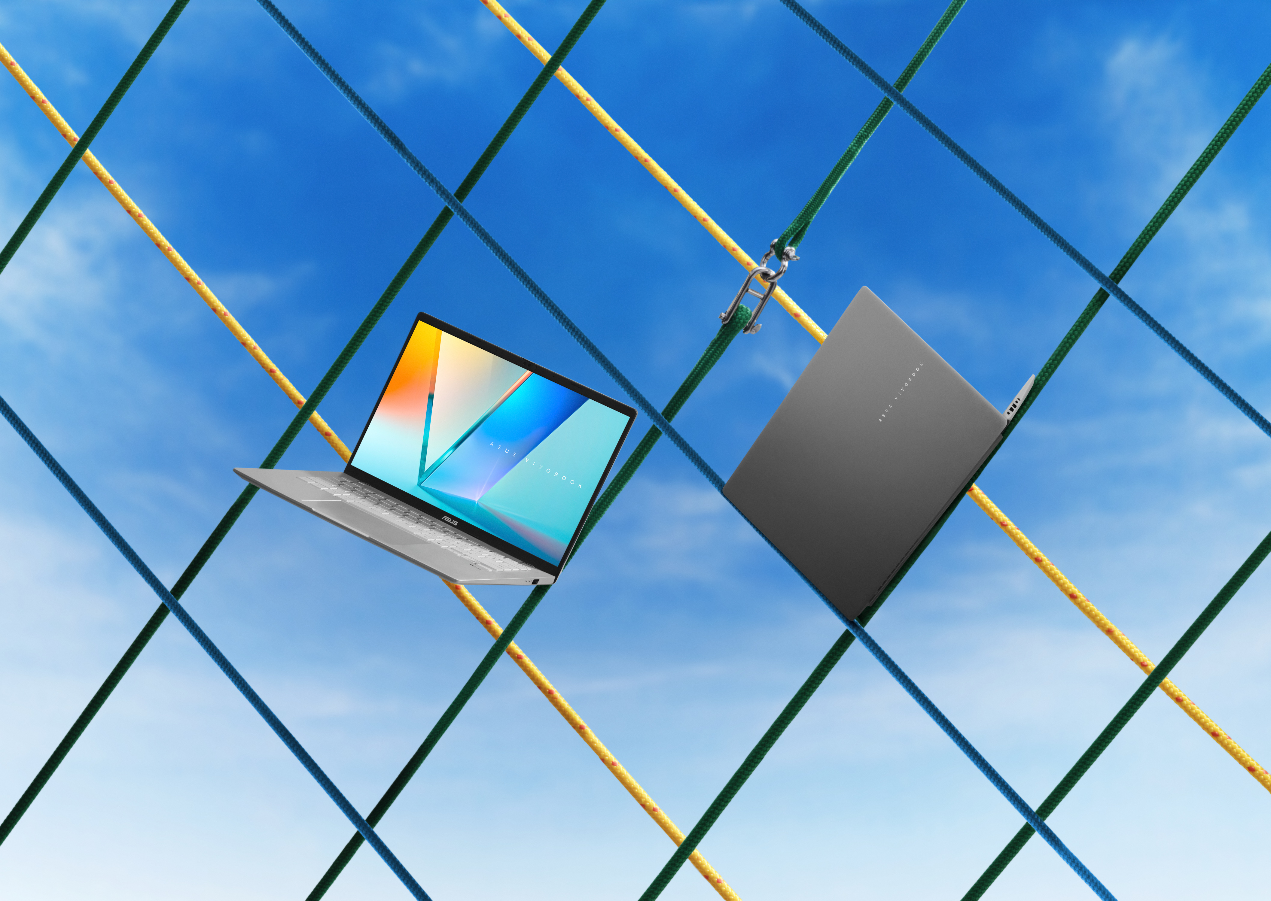 Twee laptops zweven tegen een blauwe lucht, doorkruist door kleurrijke touwen.