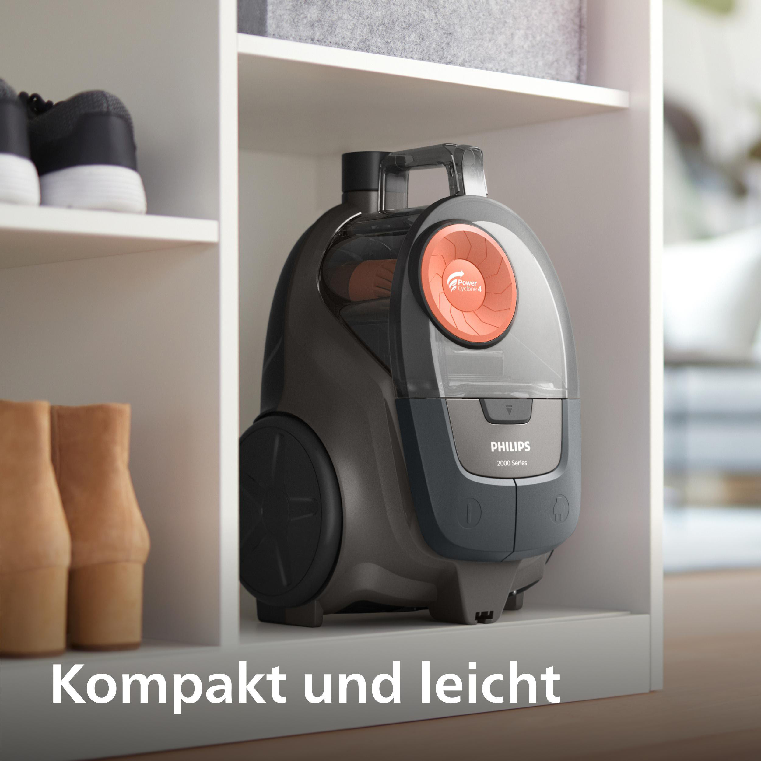 Ein kompakter, grauer Philips Staubsauger auf einem Regal neben Schuhen und Stiefeln.