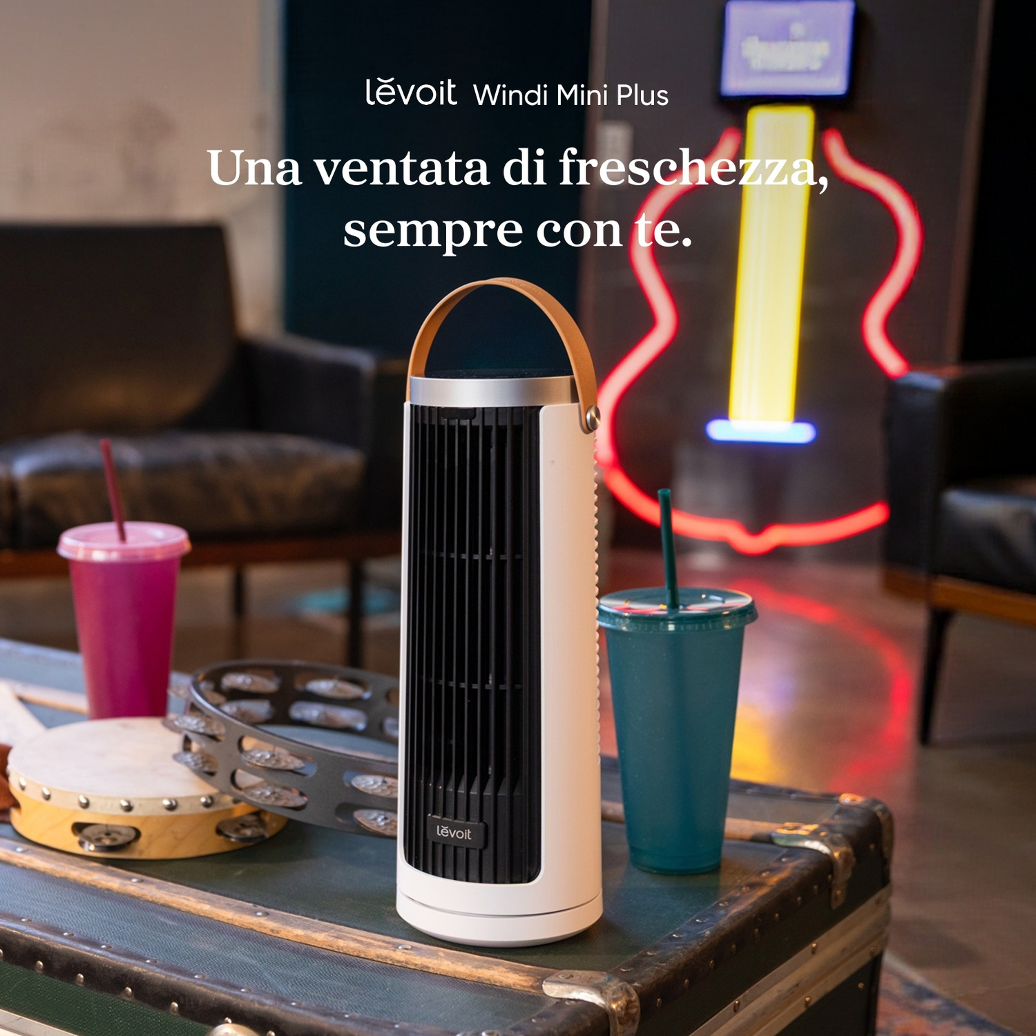 Un ventilatore a torre bianco è su un baule accanto a due bicchieri e tamburelli.