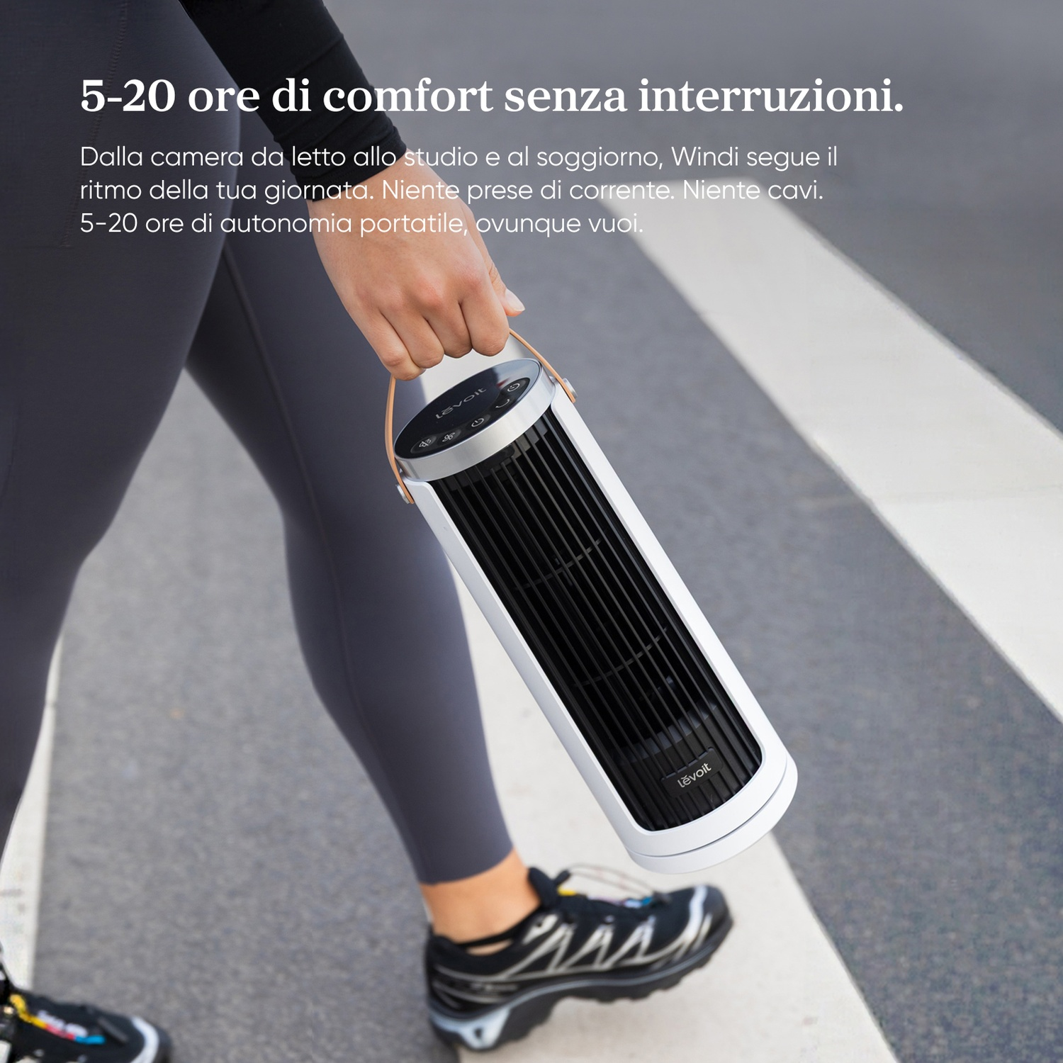 Una persona tiene un ventilatore bianco portatile con griglia nera e manico in pelle.