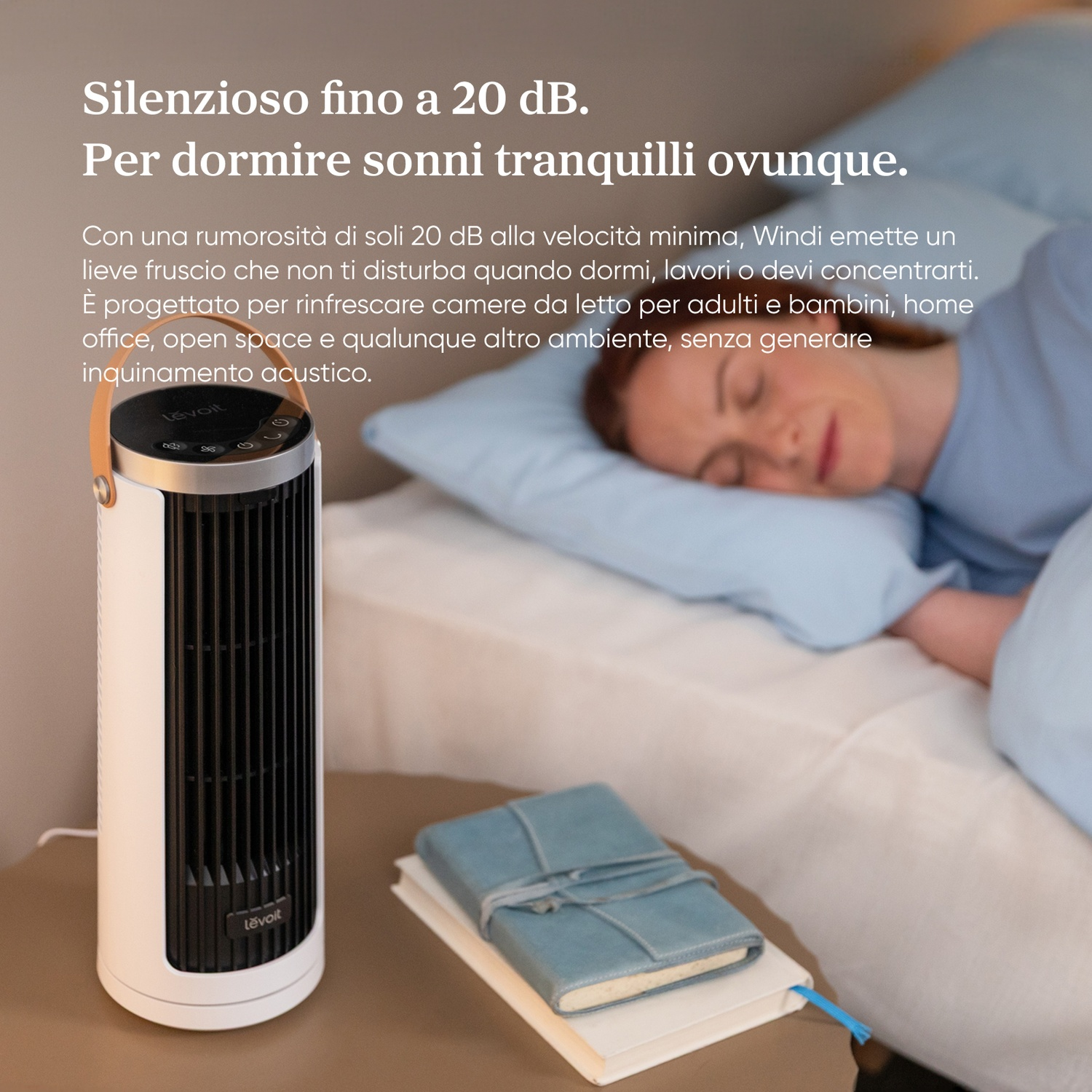 Un ventilatore a torre bianco accanto a un letto dove dorme una donna.