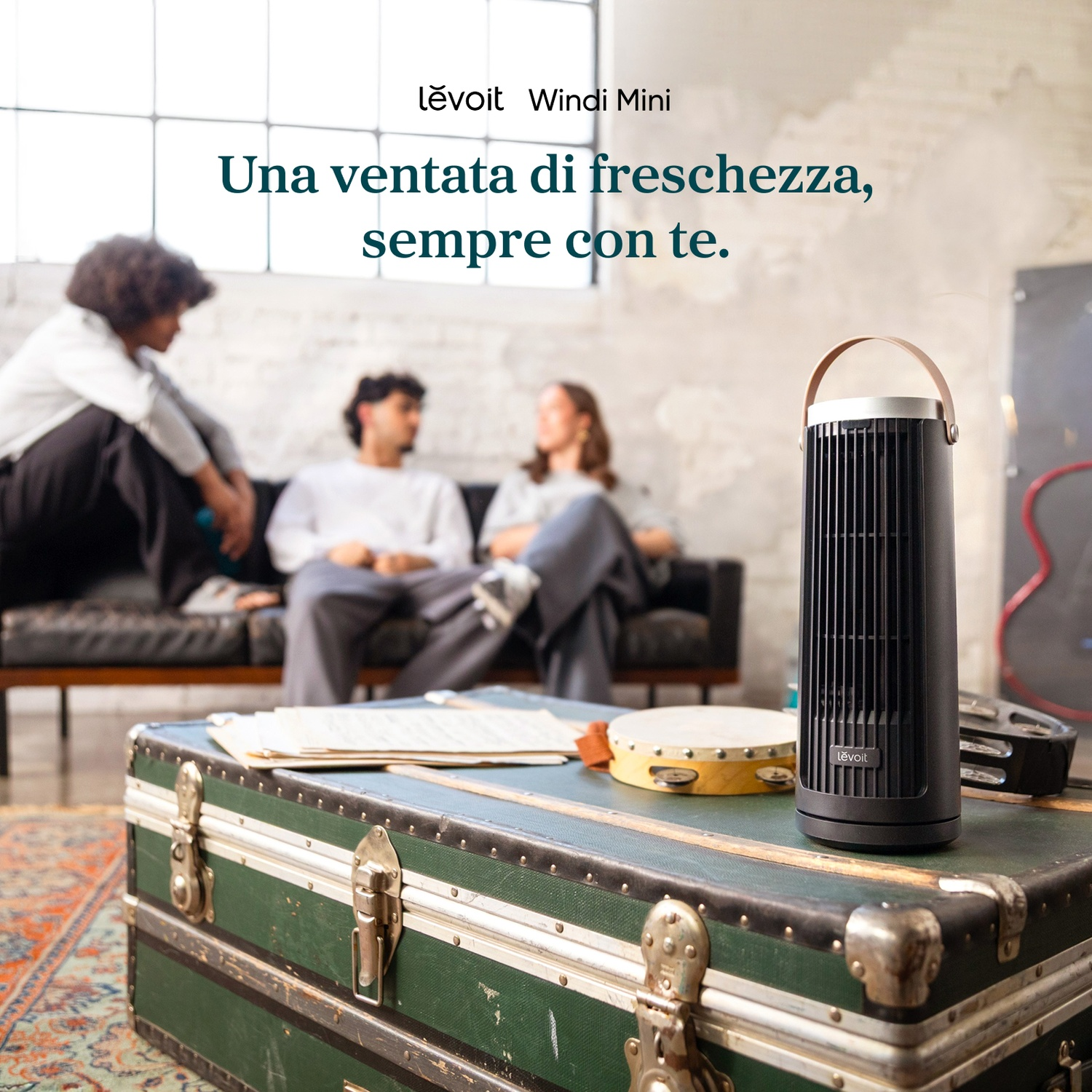 Un ventilatore Levoit su un baule verde. Tre persone sedute sullo sfondo.
