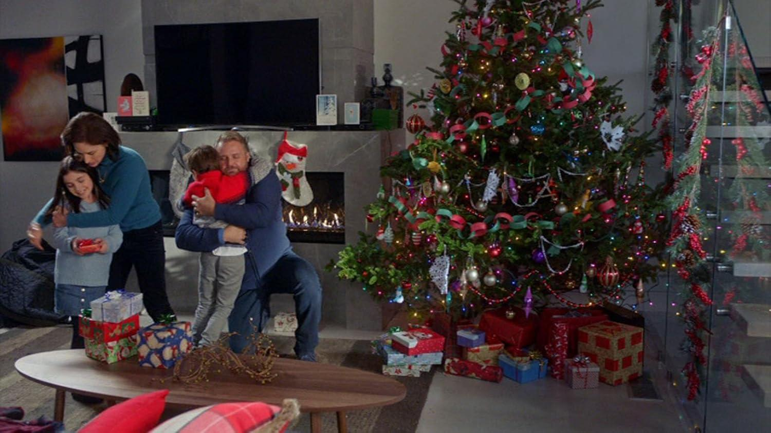 Familie umarmt sich vor einem geschmückten Weihnachtsbaum mit Geschenken und einem Kamin.
