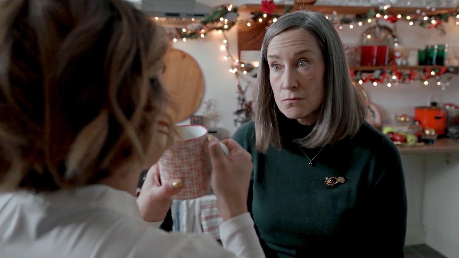 Zwei Frauen in einer Küche mit Weihnachtslichtern. Eine hält eine Tasse.