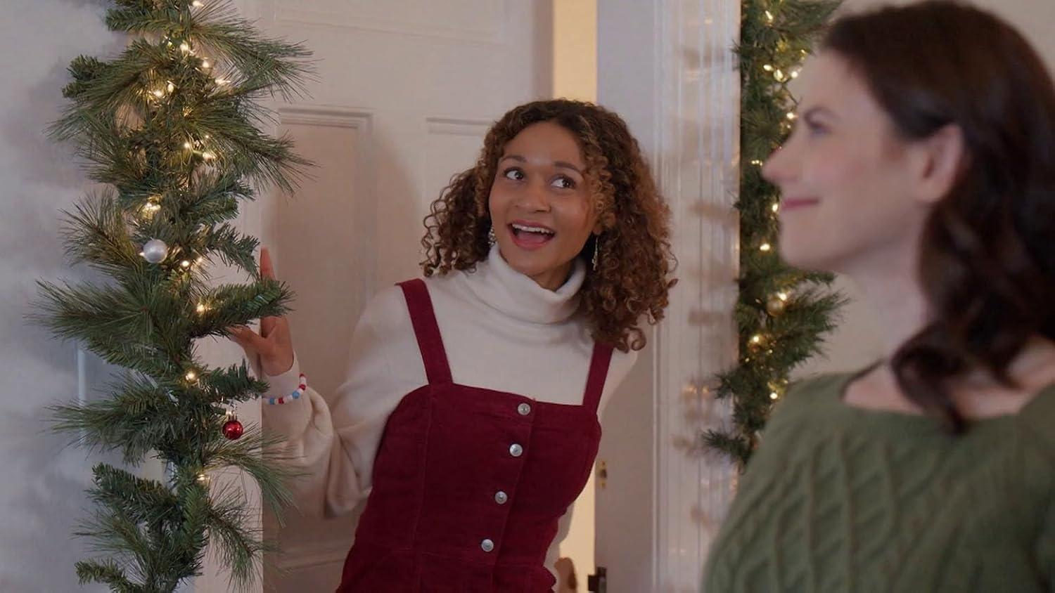 Eine Frau im roten Kleid und weißem Rollkragen lächelt in der Nähe eines Weihnachtsgirlande.