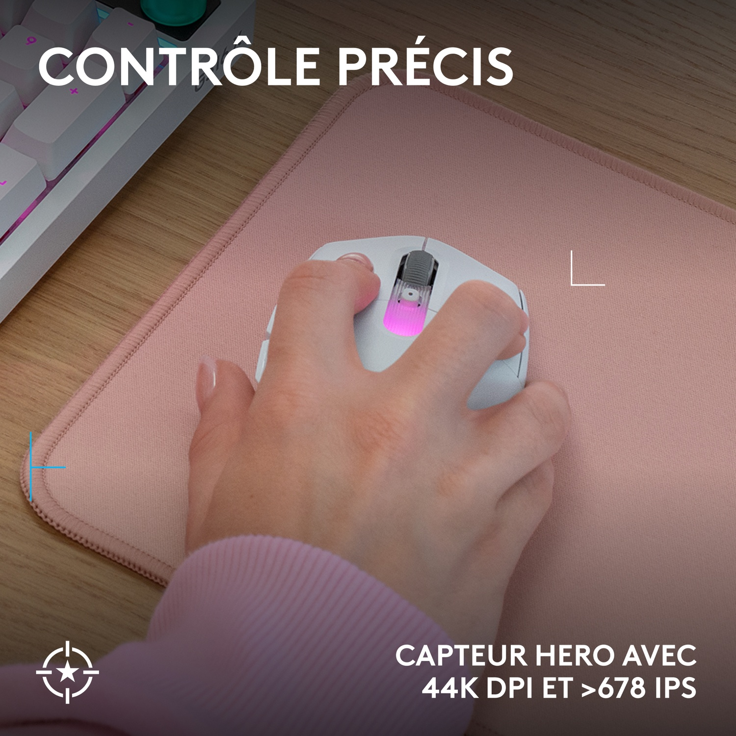 Une main utilise une souris blanche sur un tapis rose. Clavier en arrière-plan.