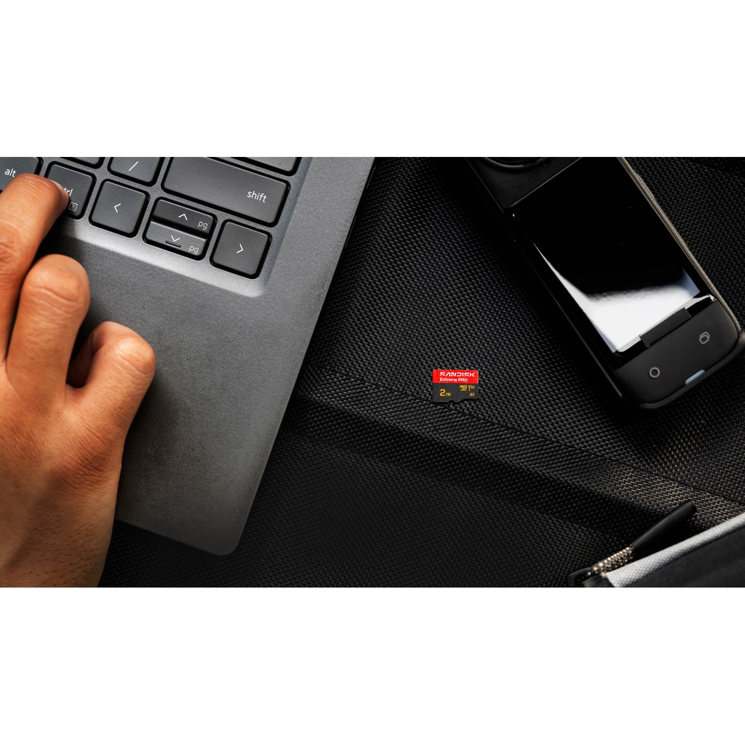 Una mano toca el teclado de un portátil, junto a un smartphone y una tarjeta de memoria.