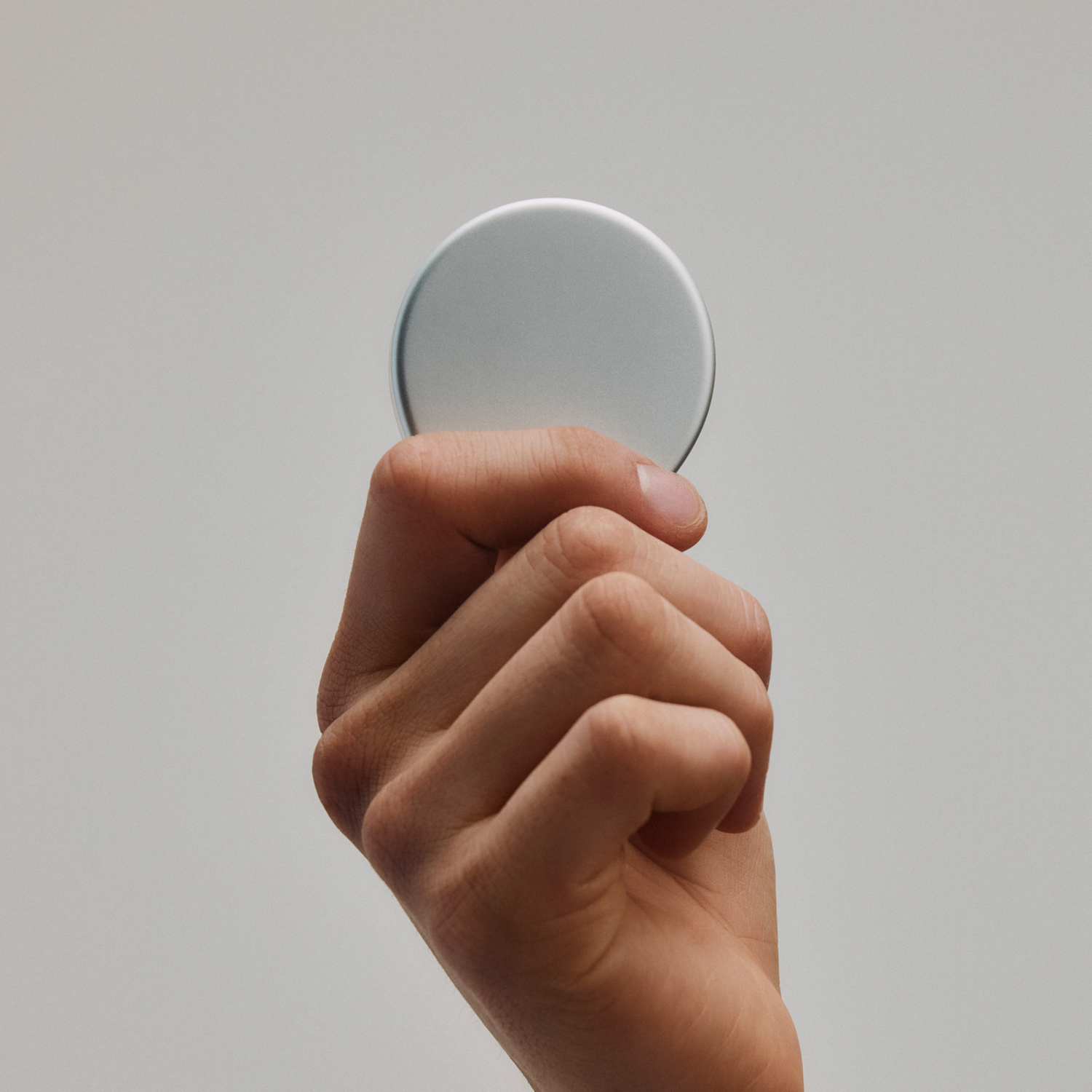 Una mano sostiene un objeto circular plateado sobre un fondo gris liso.