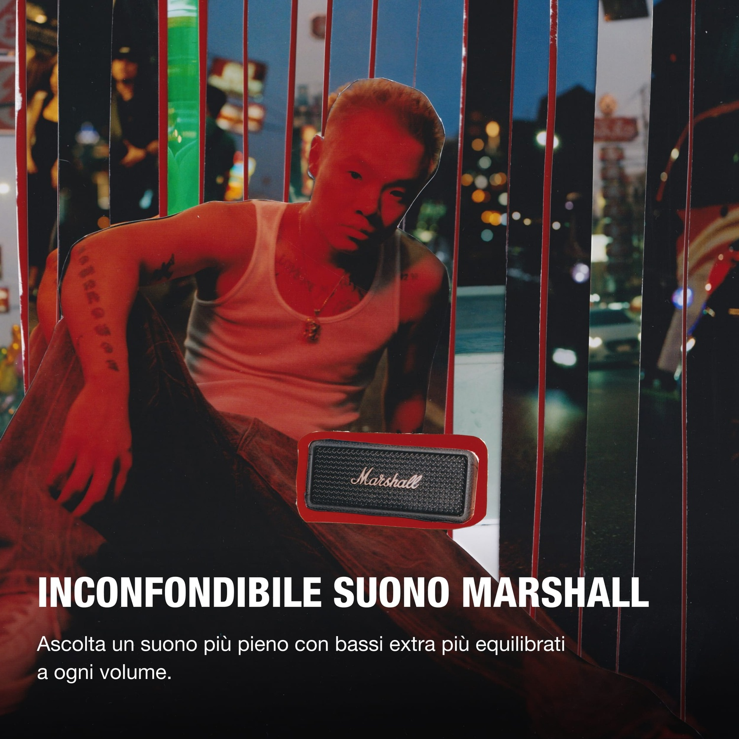 Uomo con tatuaggi seduto con altoparlante Marshall su sfondo città notturna.