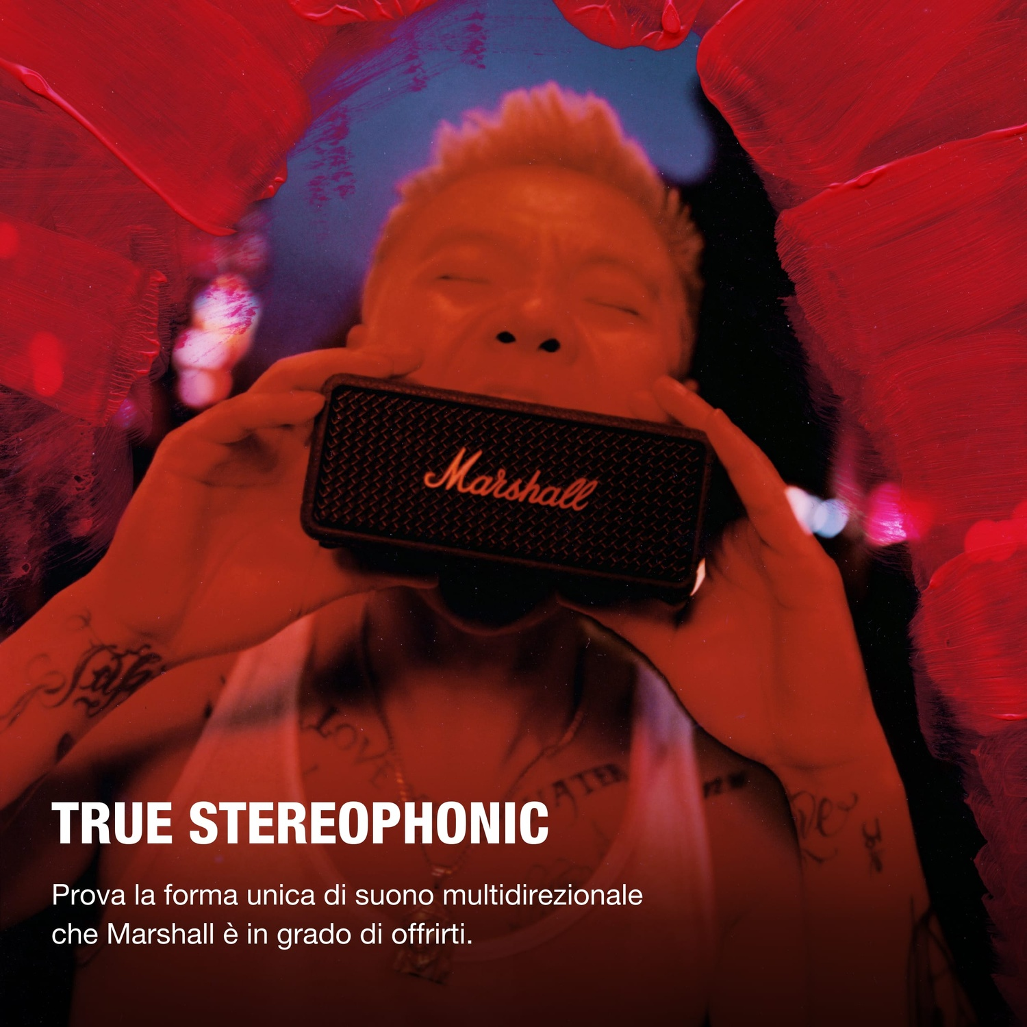 Persona tiene altoparlante Marshall alla bocca, circondata da vernice rossa e sfondo blu.