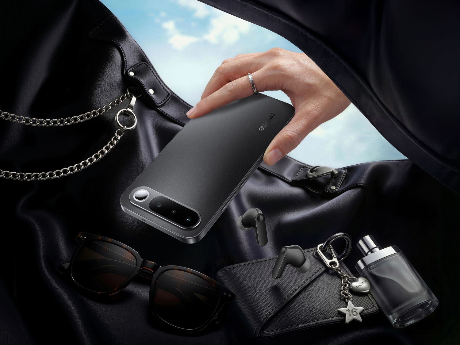 Dłoń trzyma szary smartfon nad czarną skórzaną torbą z akcesoriami.