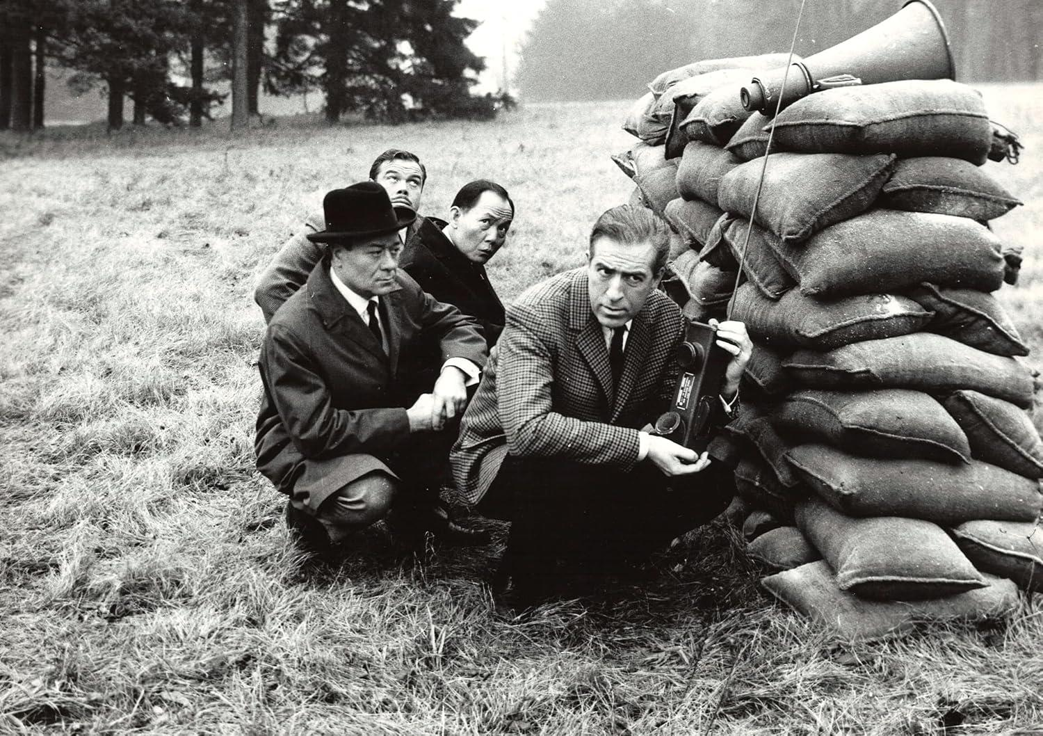Vier Männer knien vor einem Stapel Sandsäcke. Einer hält ein Funkgerät.