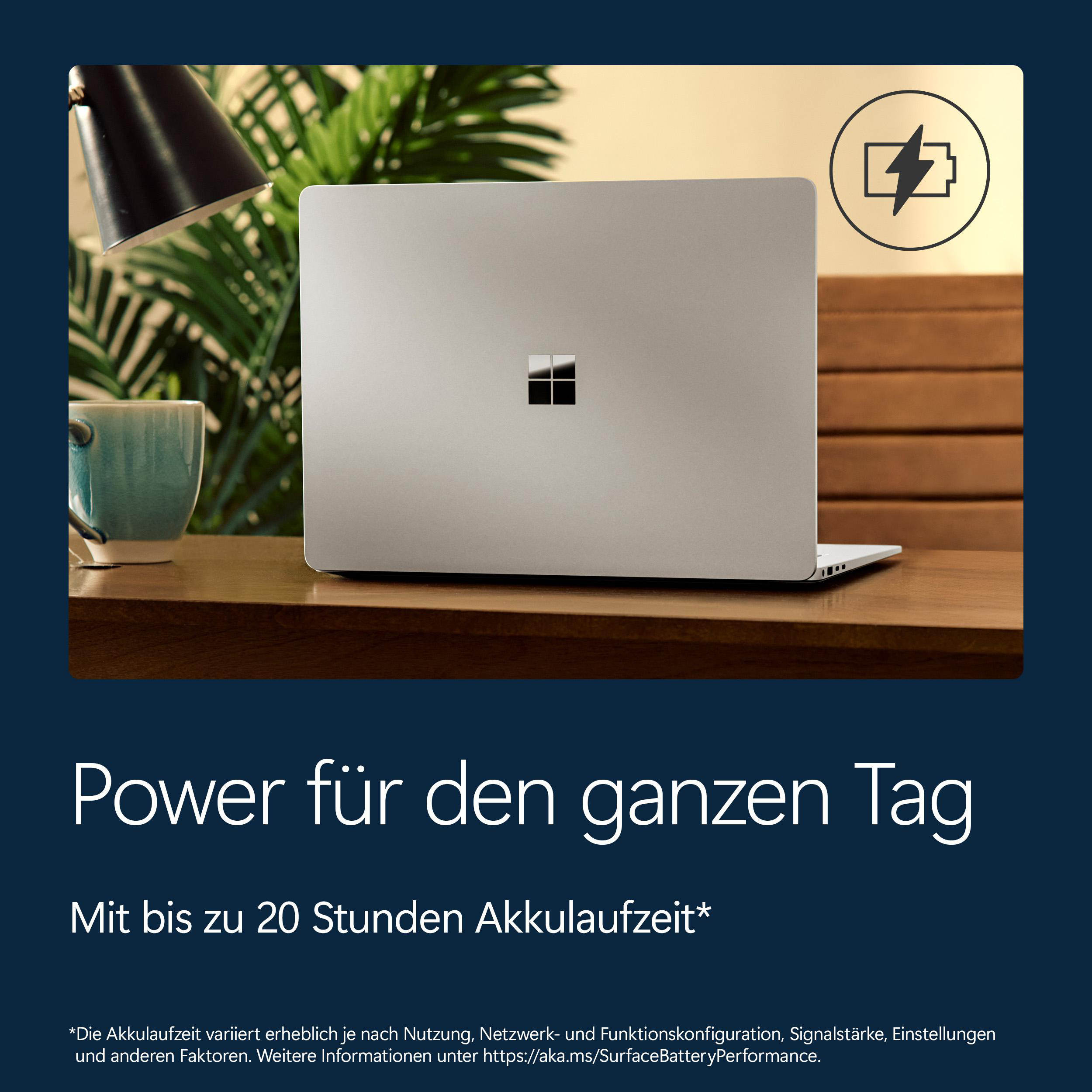 Ein silberner Laptop mit einem Akku-Symbol. Im Vordergrund eine Tasse und eine Lampe.