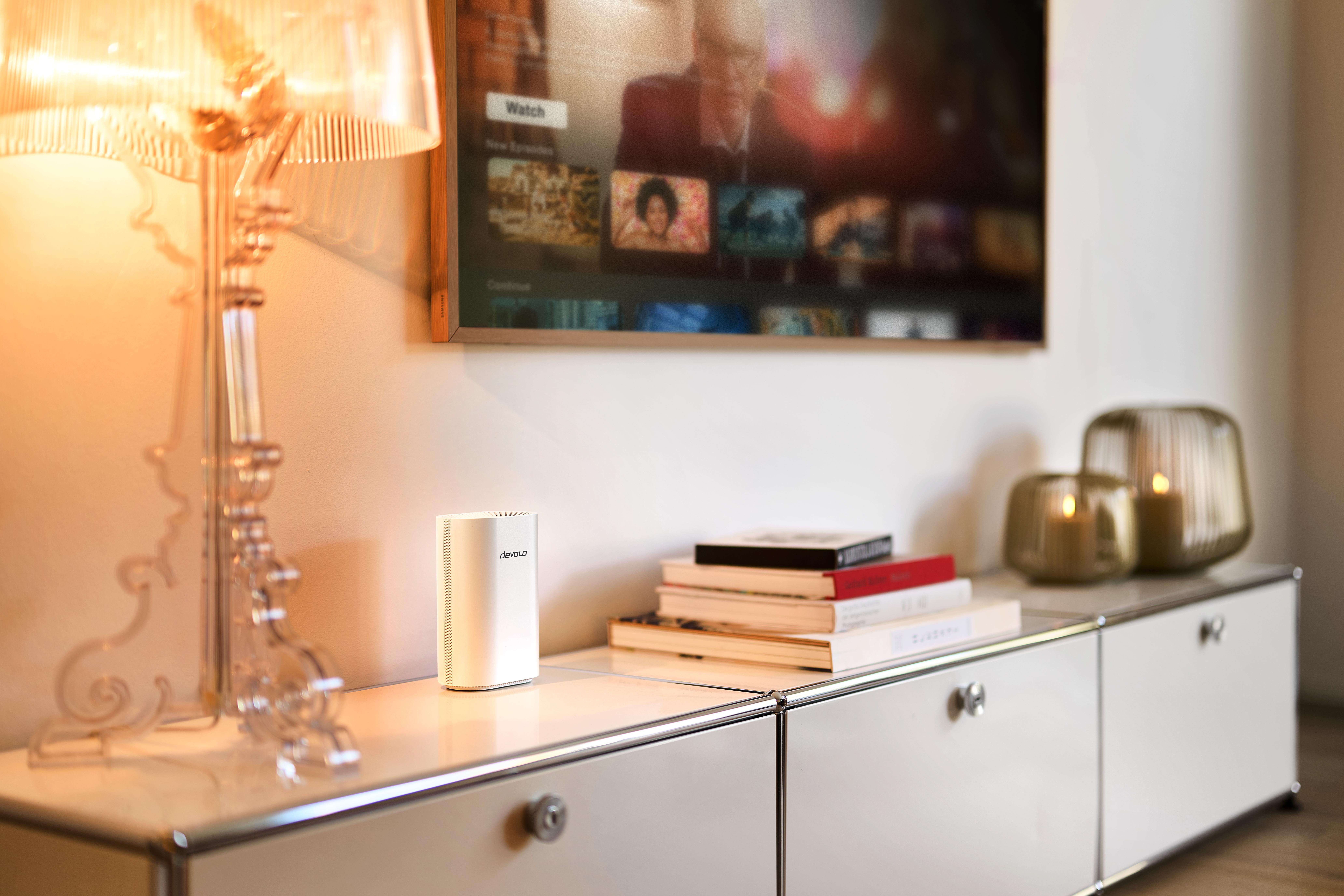 Ein weißer Router steht auf einem weißen Sideboard neben Büchern und Kerzen.