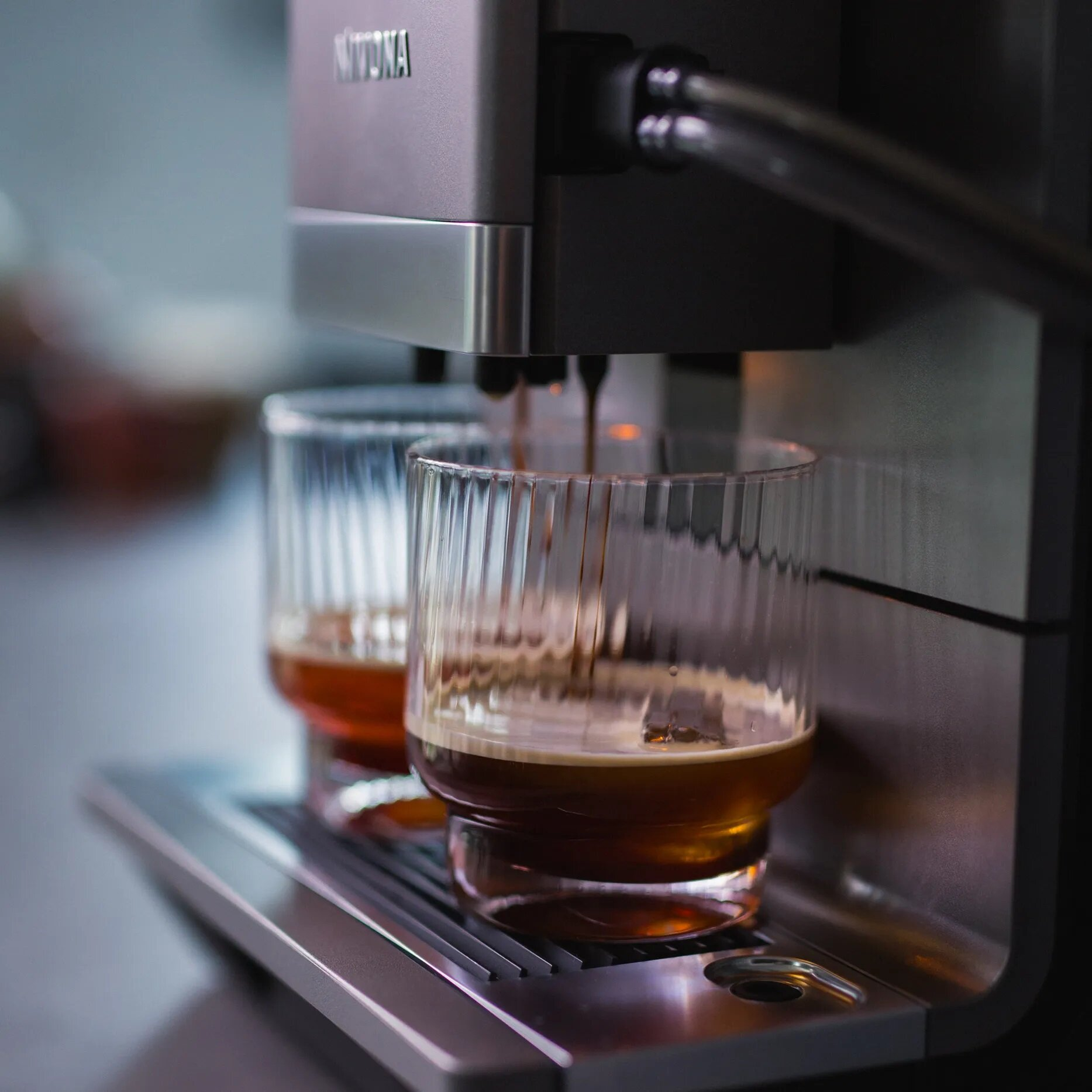 Ekspres do kawy parzy espresso do dwóch szklanych kubków z rowkami.