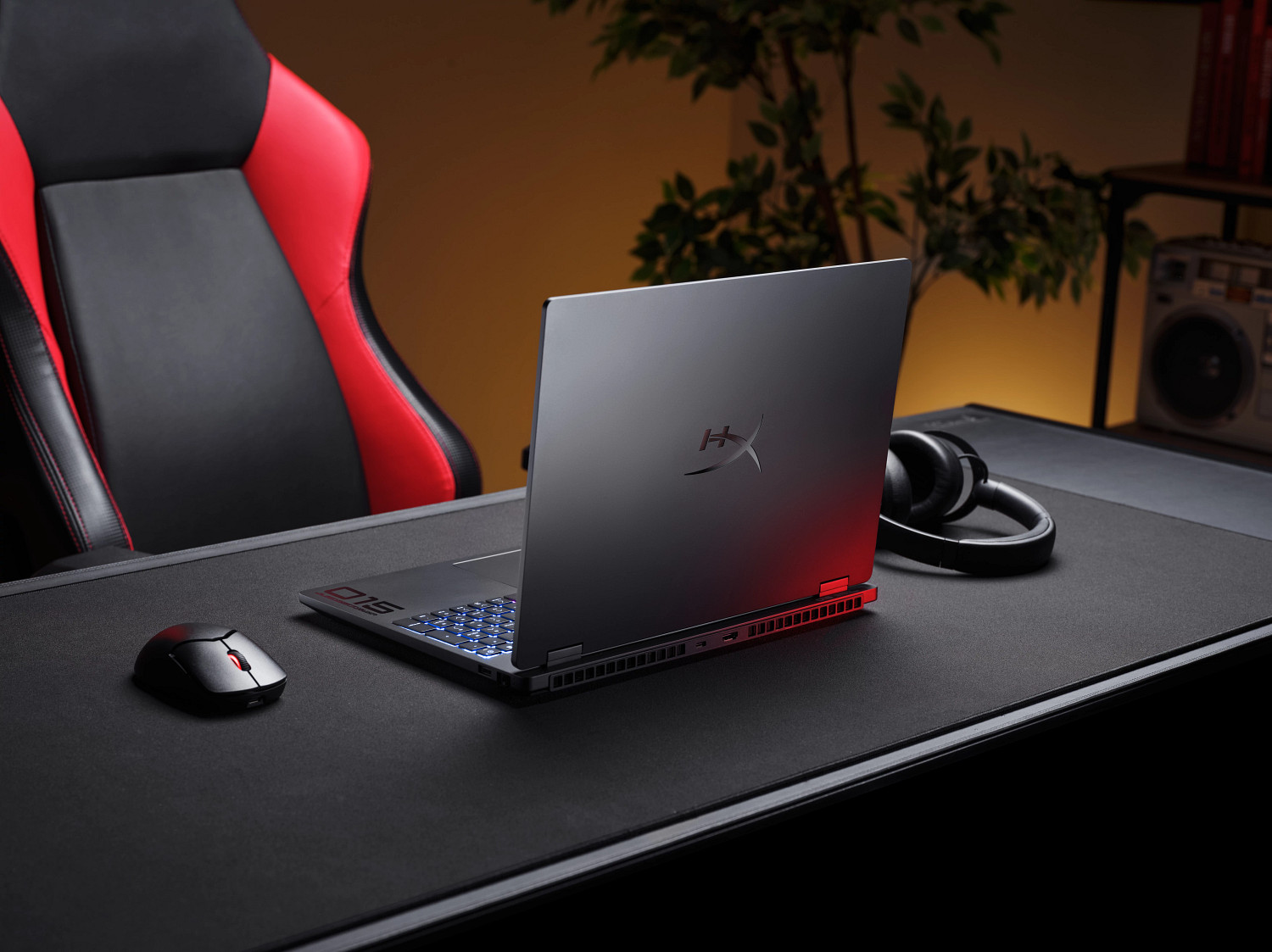 Laptop gamingowy z czerwonym podświetleniem, myszką, słuchawkami i czerwono-czarnym fotelem.