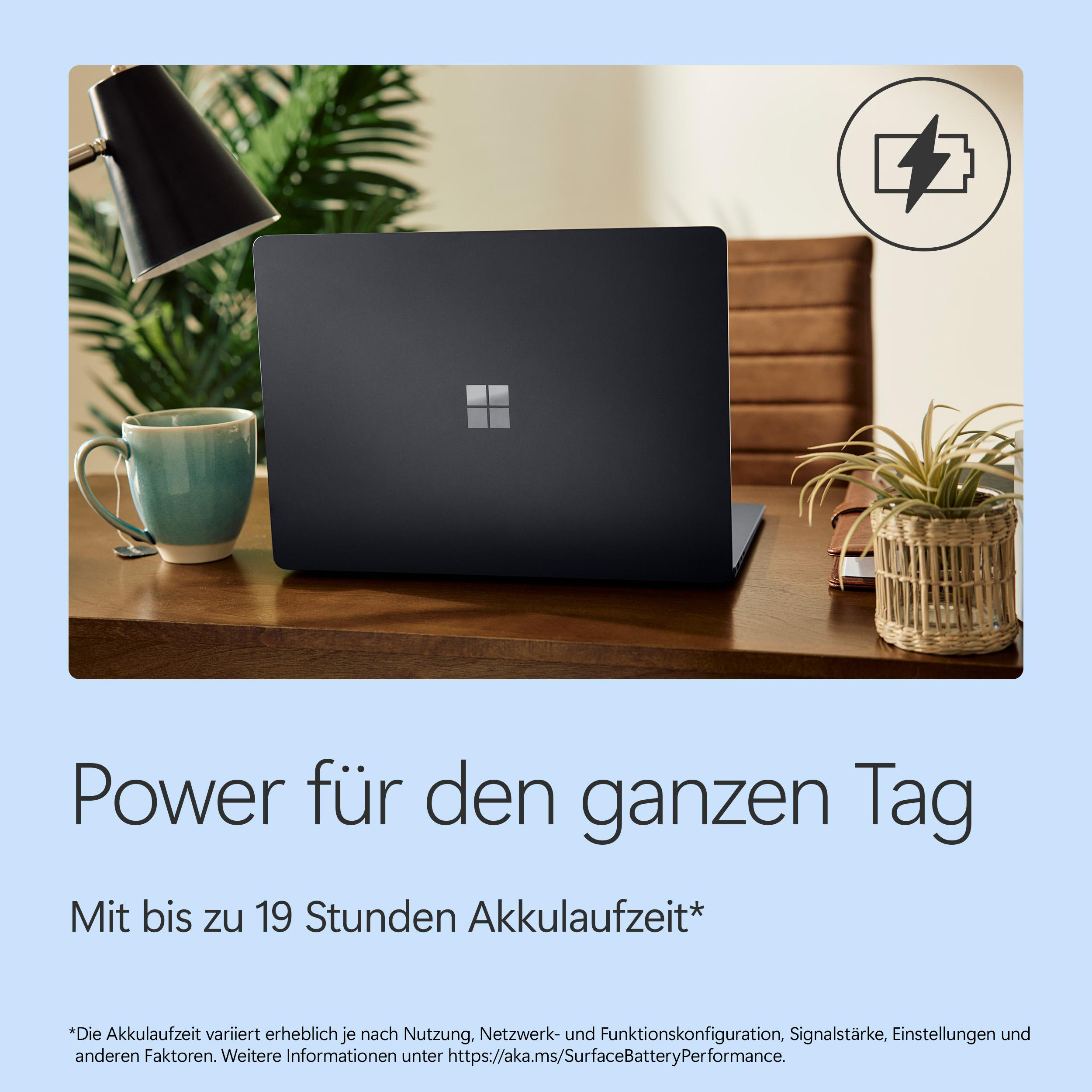 Ein dunkles Laptop steht auf einem Holzschreibtisch. Links eine Tasse, rechts eine Pflanze.