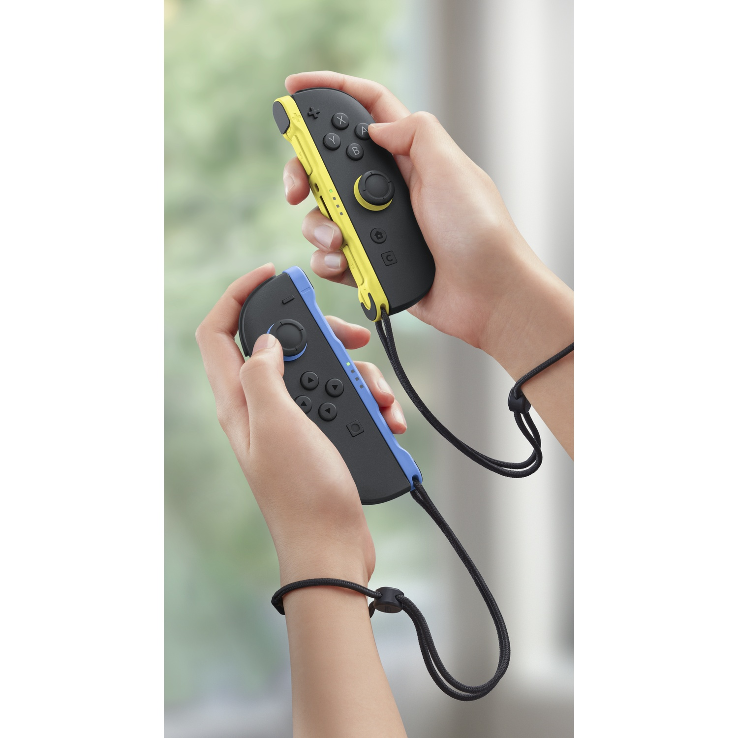 Mains tenant des manettes Joy-Con jaunes et bleues avec dragonnes.