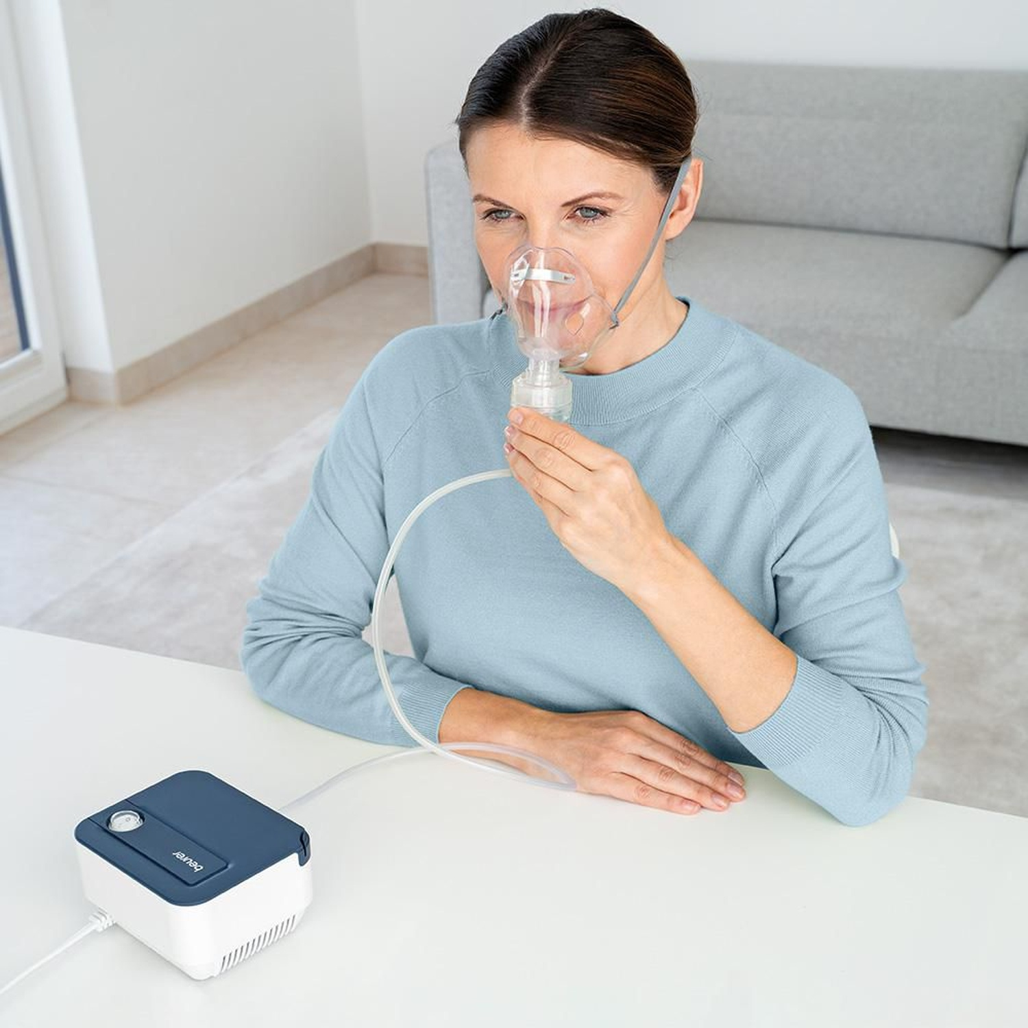 Donna con maschera nebulizzatrice seduta a un tavolo. Un nebulizzatore accanto.