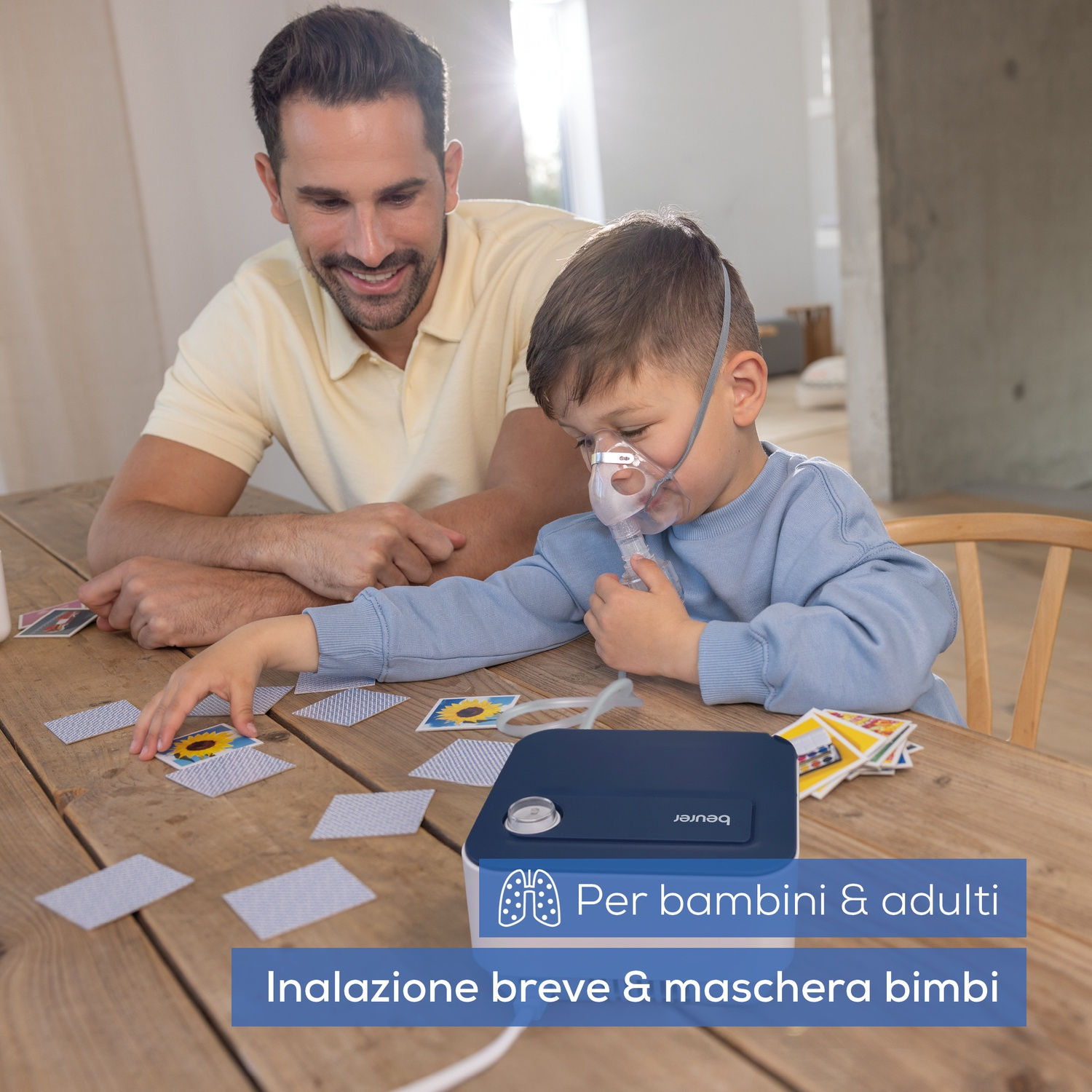 Padre e figlio giocano a carte. Il figlio indossa una maschera e un inalatore.