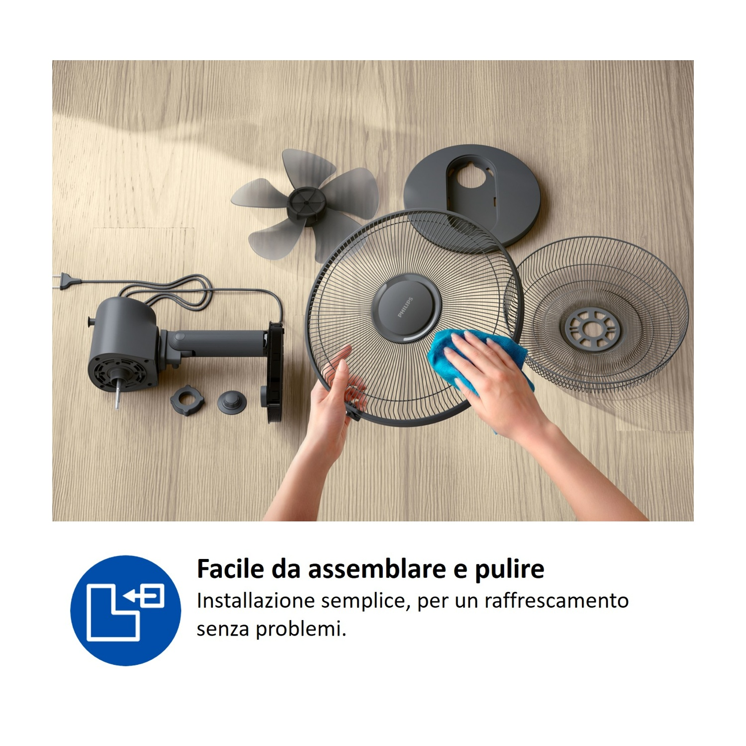Parti di un ventilatore su pavimento di legno, una mano pulisce la griglia.