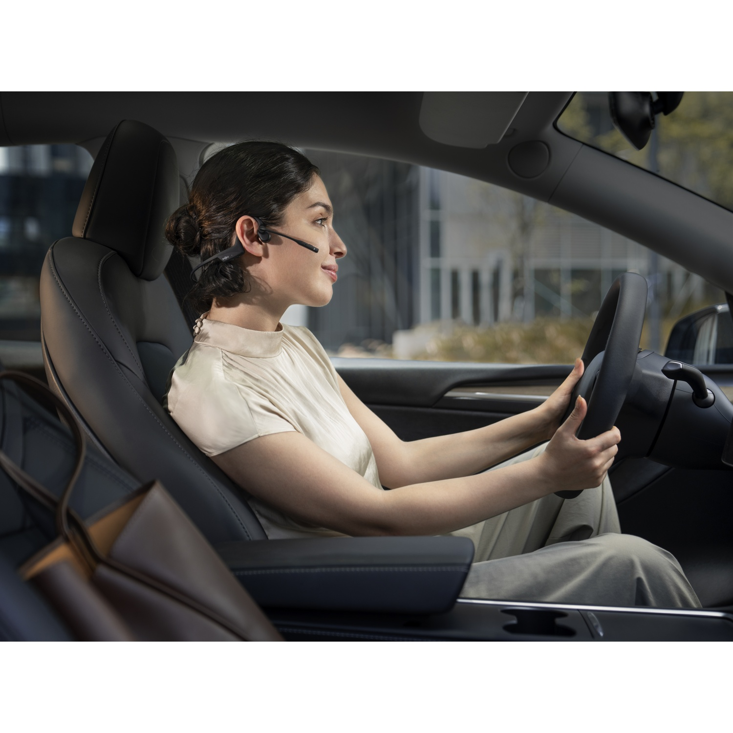 Een vrouw met headset rijdt auto, kijkt naar rechts.